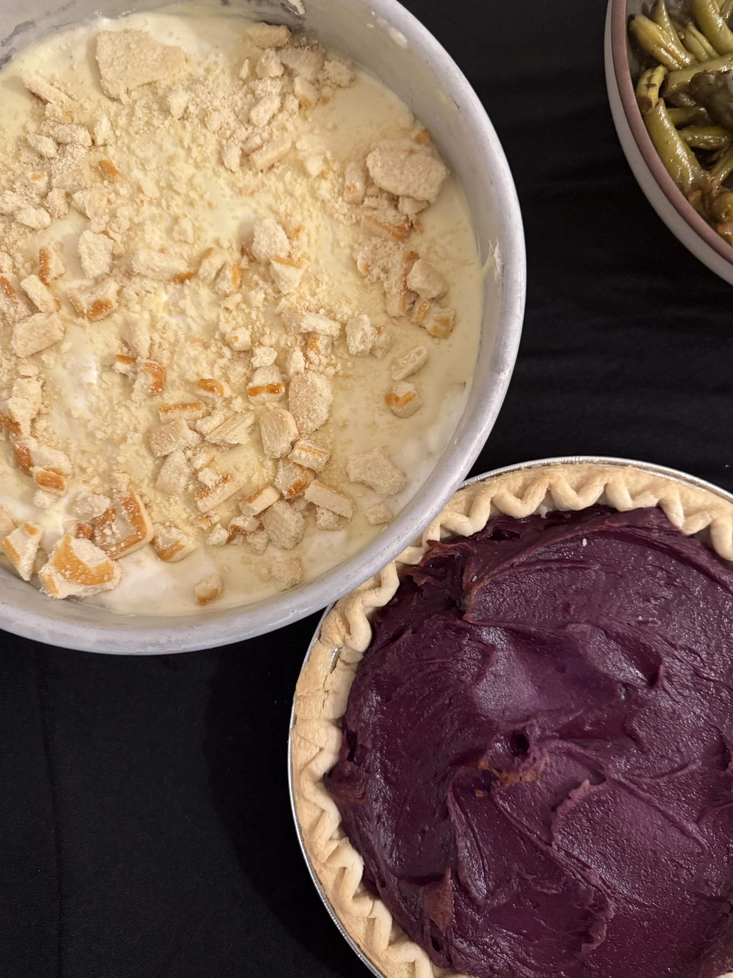 Close-up of a purple sweet potato pie with a flaky crust, and a plantain pudding.