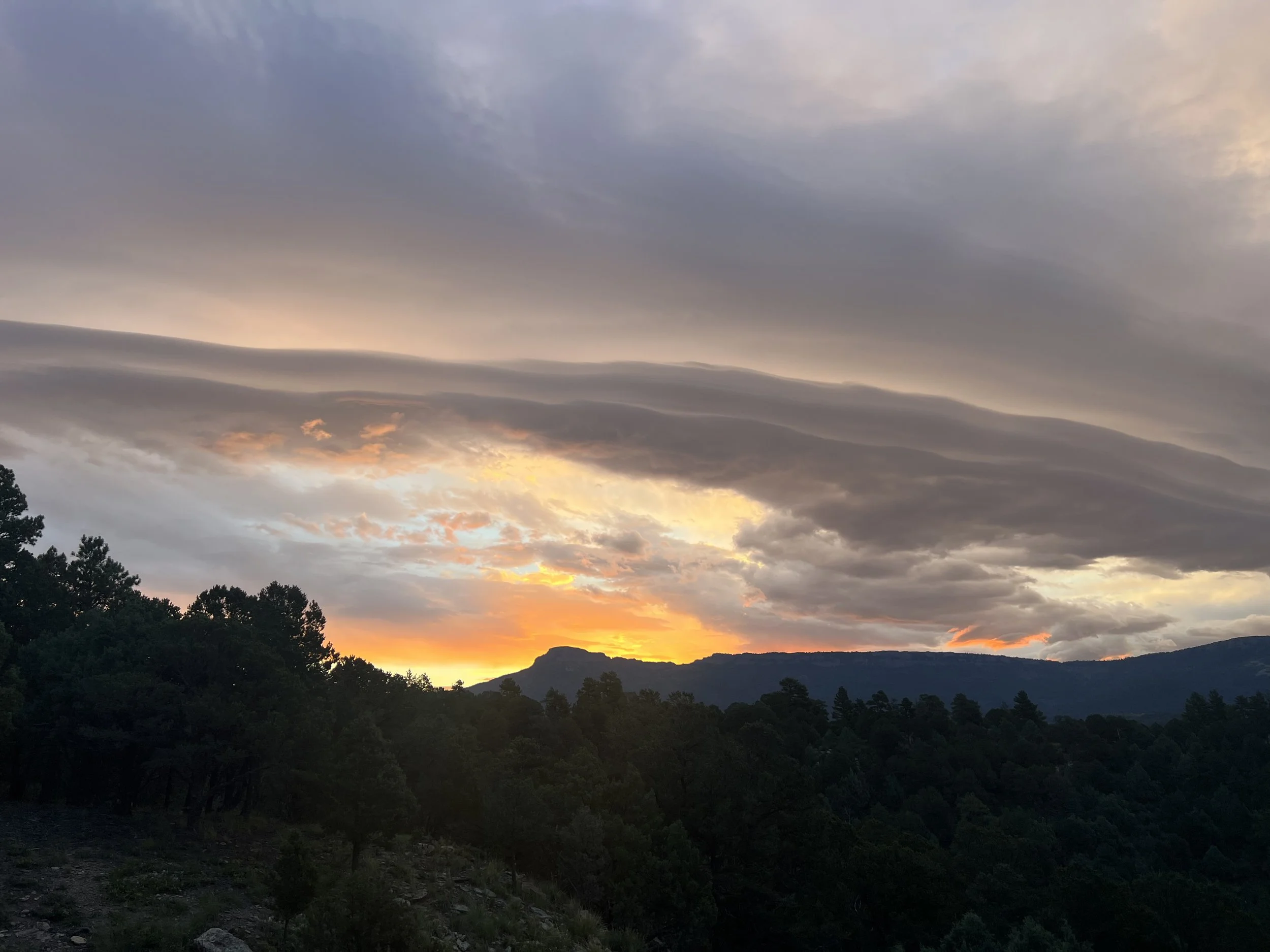 Sunset over a forested mountain landscape with cloudy sky.