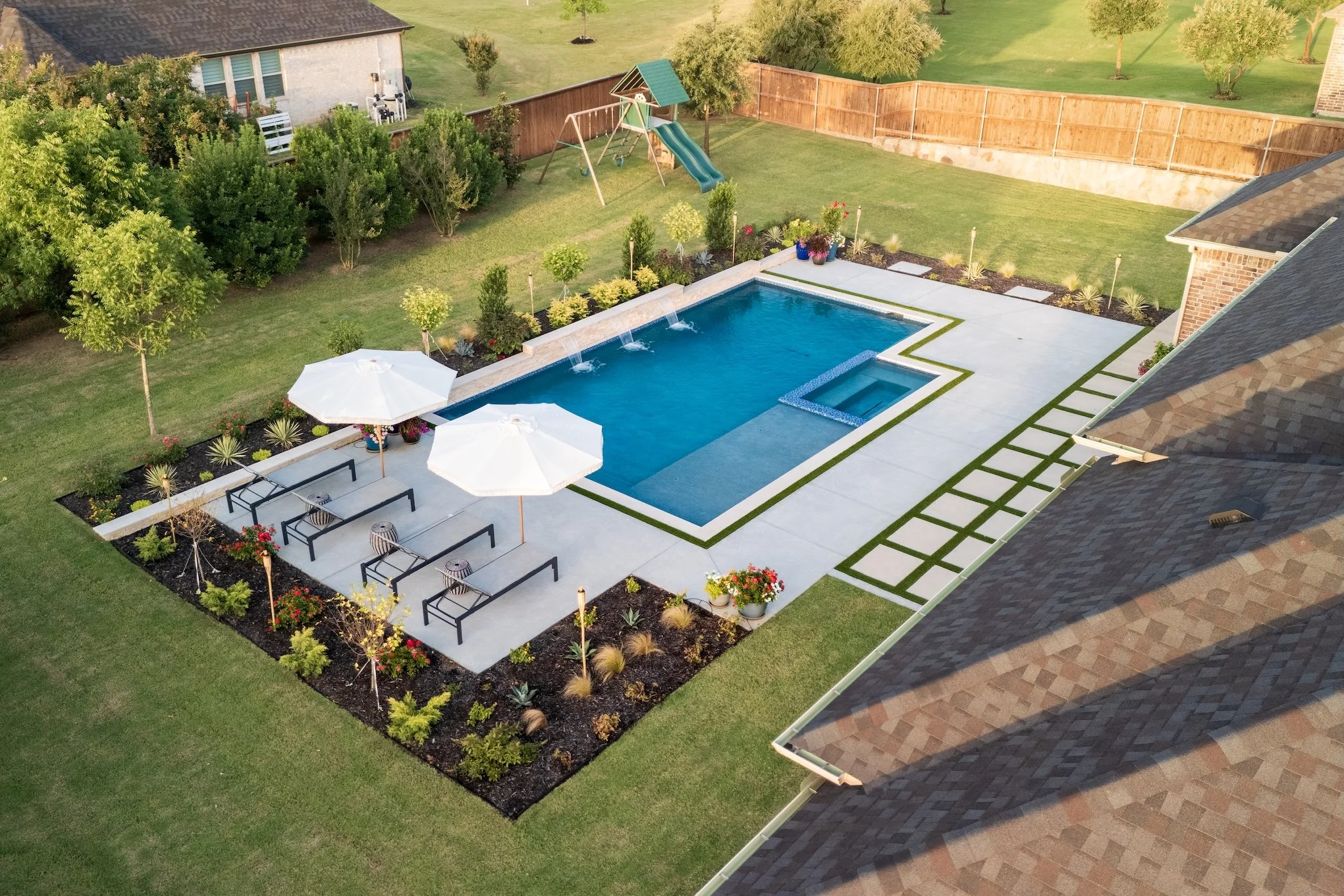 swimming pool and spa with hot tub, tanning ledge, waterfalls, decking, and landscaping in Keller