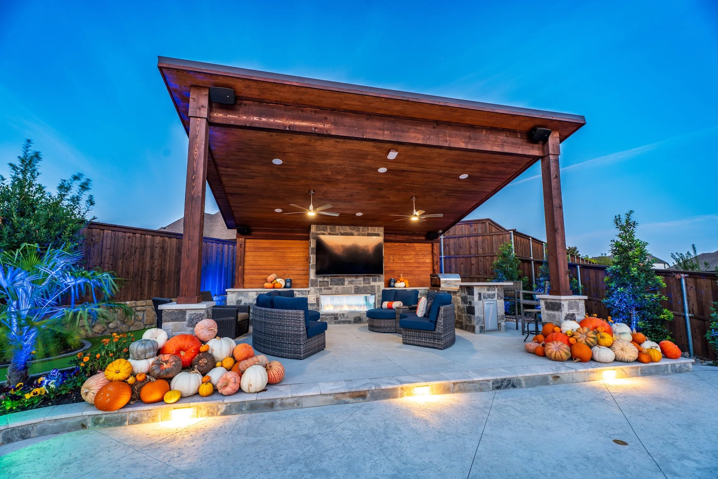 Outdoor patio with a covered wood ceiling, outdoor seating, and a stone fireplace surrounded by pumpkins for fall decor.