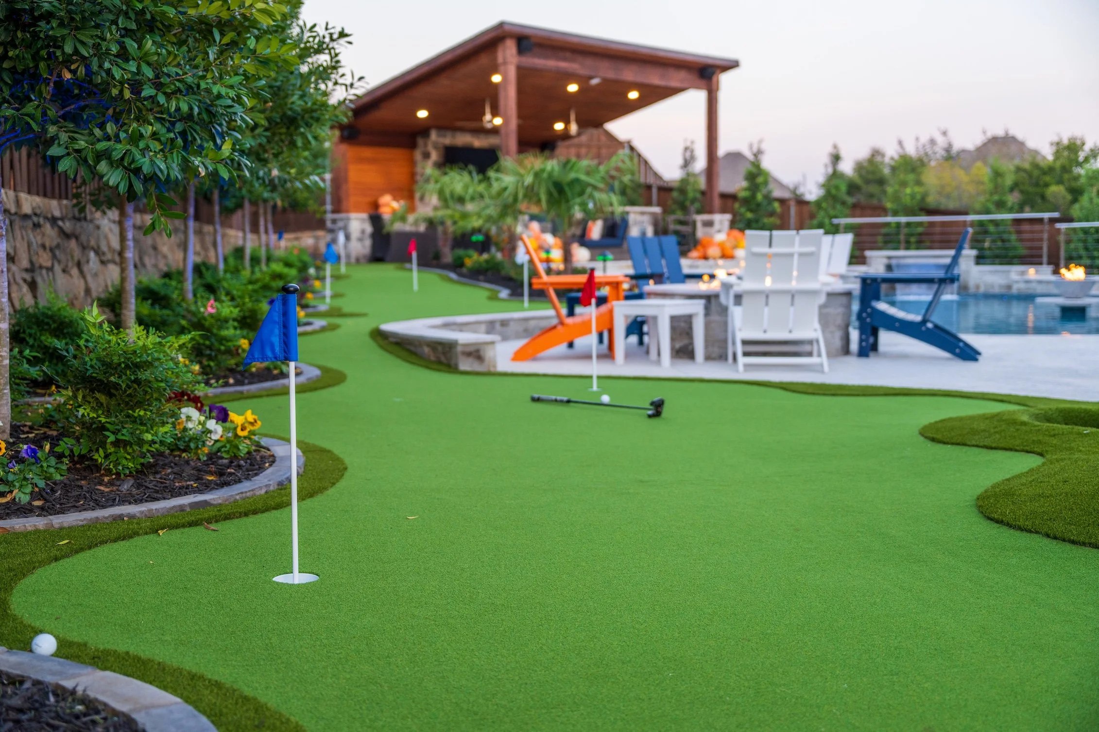 Backyard with mini-golf course, putting green, and pool area with lounge chairs, umbrellas, and covered patio.