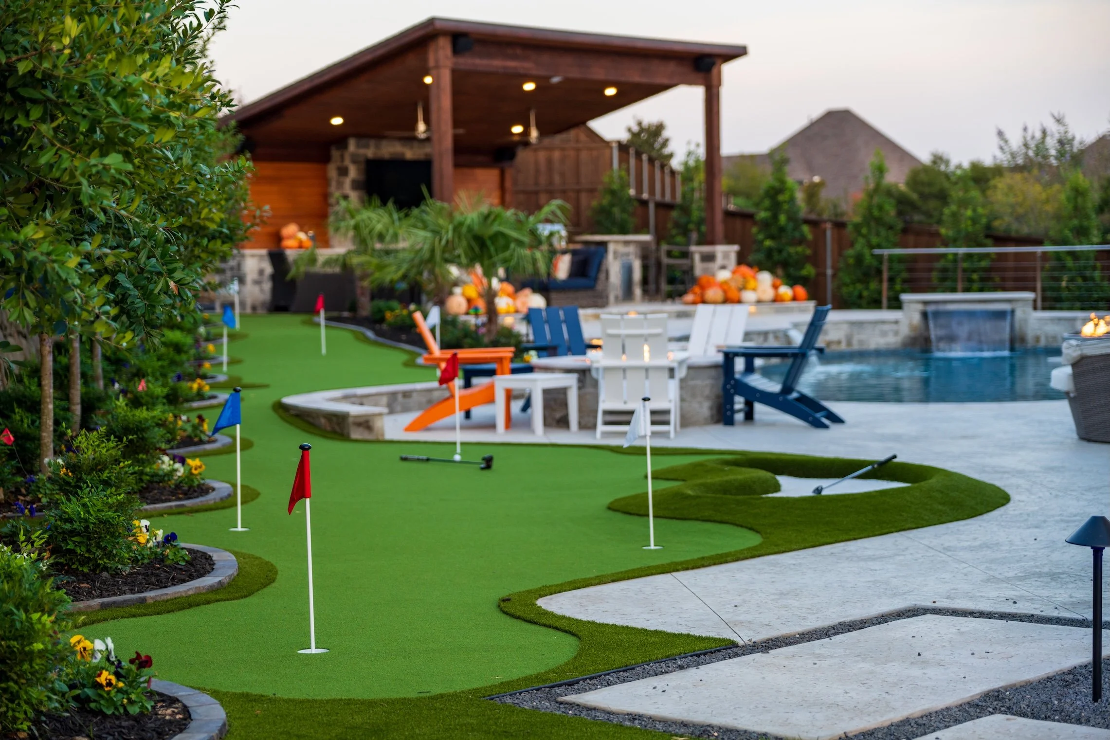 Backyard with a mini golf course, patio with Adirondack chairs, pool, and surrounding lush greenery