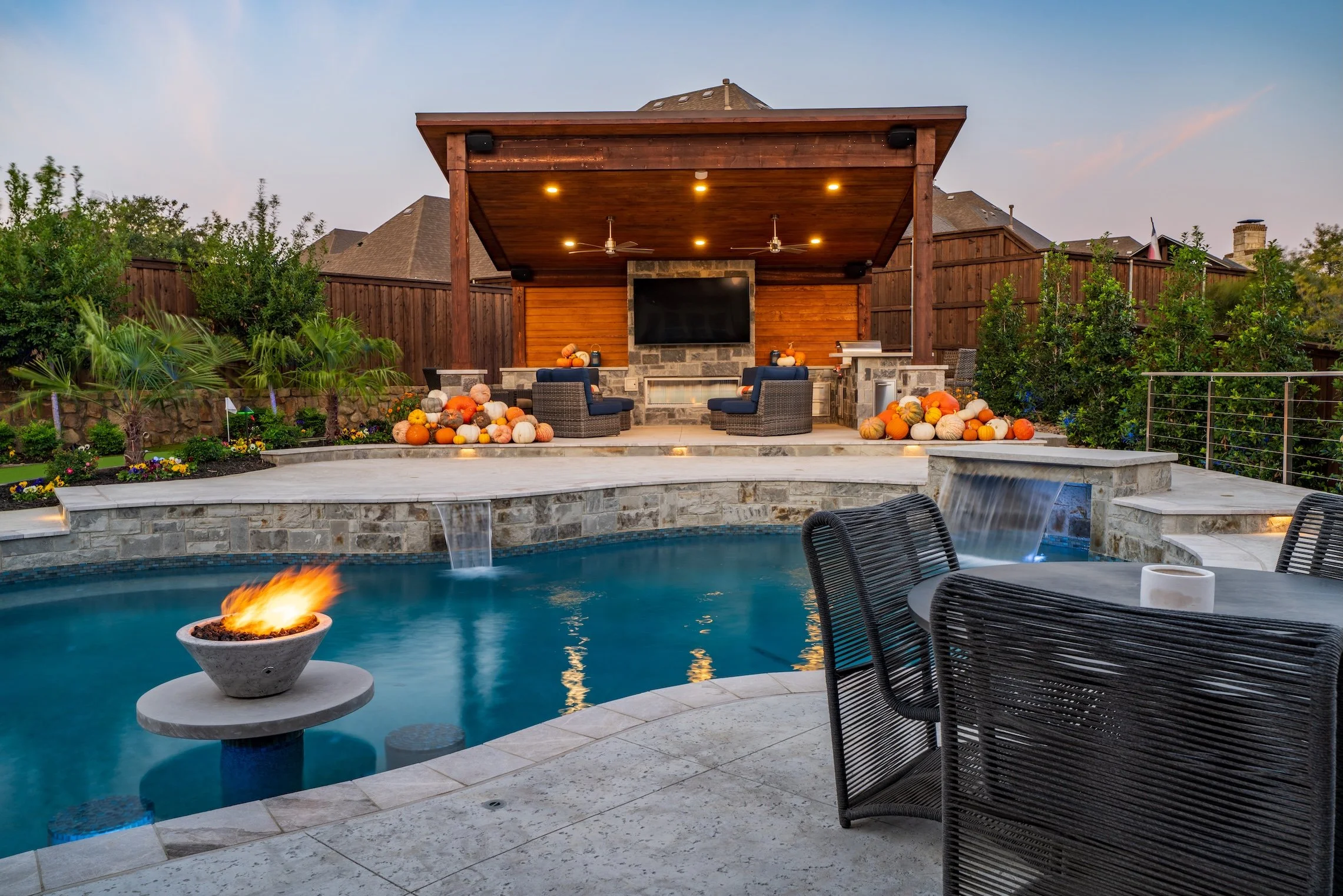 Backyard with a swimming pool, fire pit, outdoor seating, a covered patio with a TV, and pumpkins for fall decor.