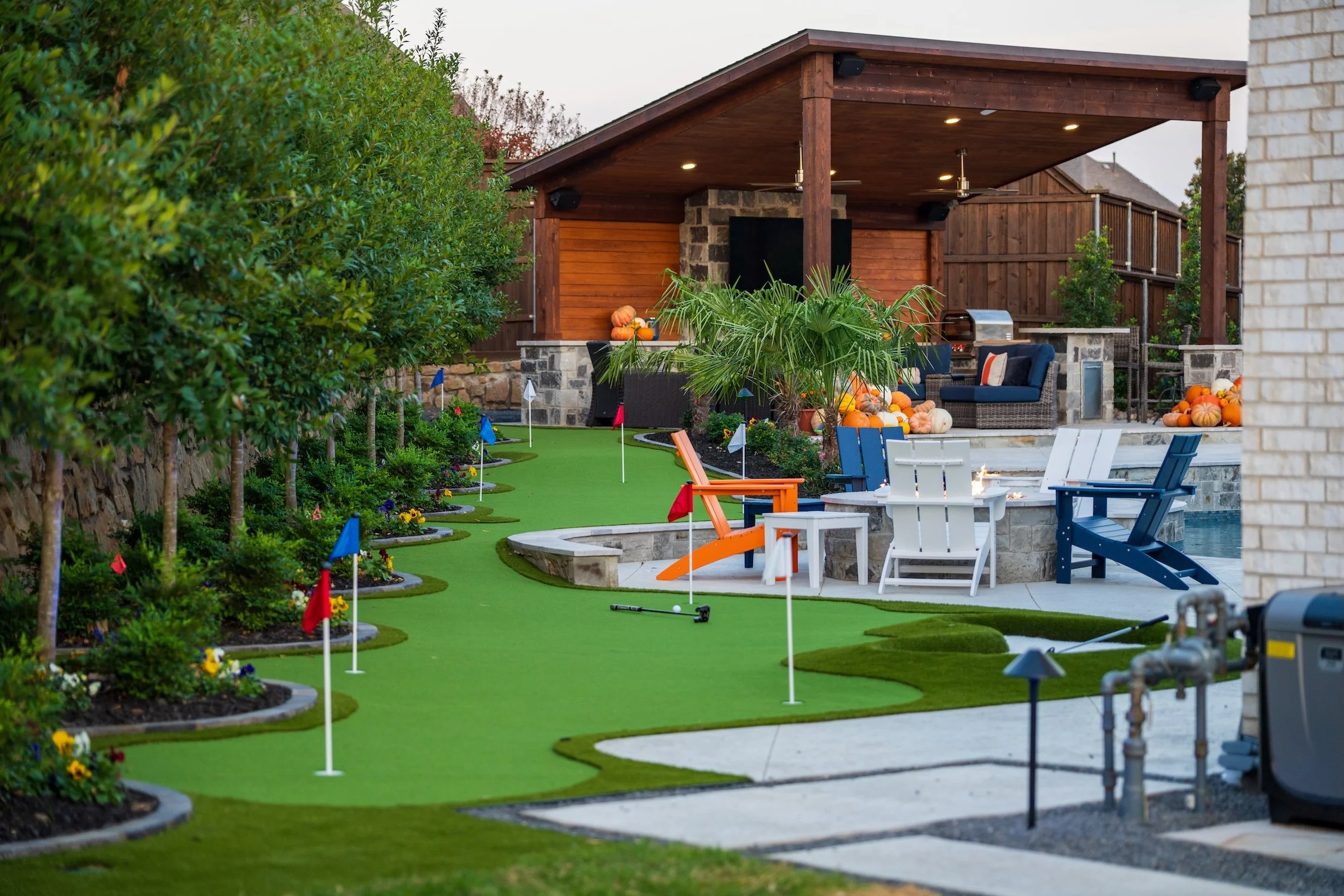 Backyard with a mini golf course, seating area, palm tree, pumpkins, and a wooden pavilion.