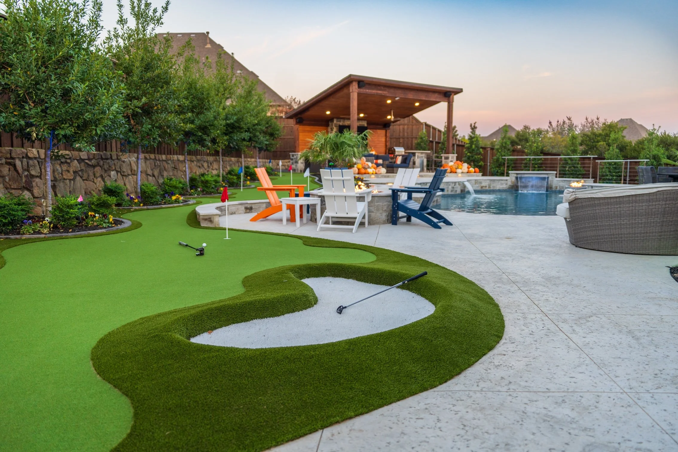 Backyard with putting green, swimming pool, outdoor seating, and a covered patio at sunset.