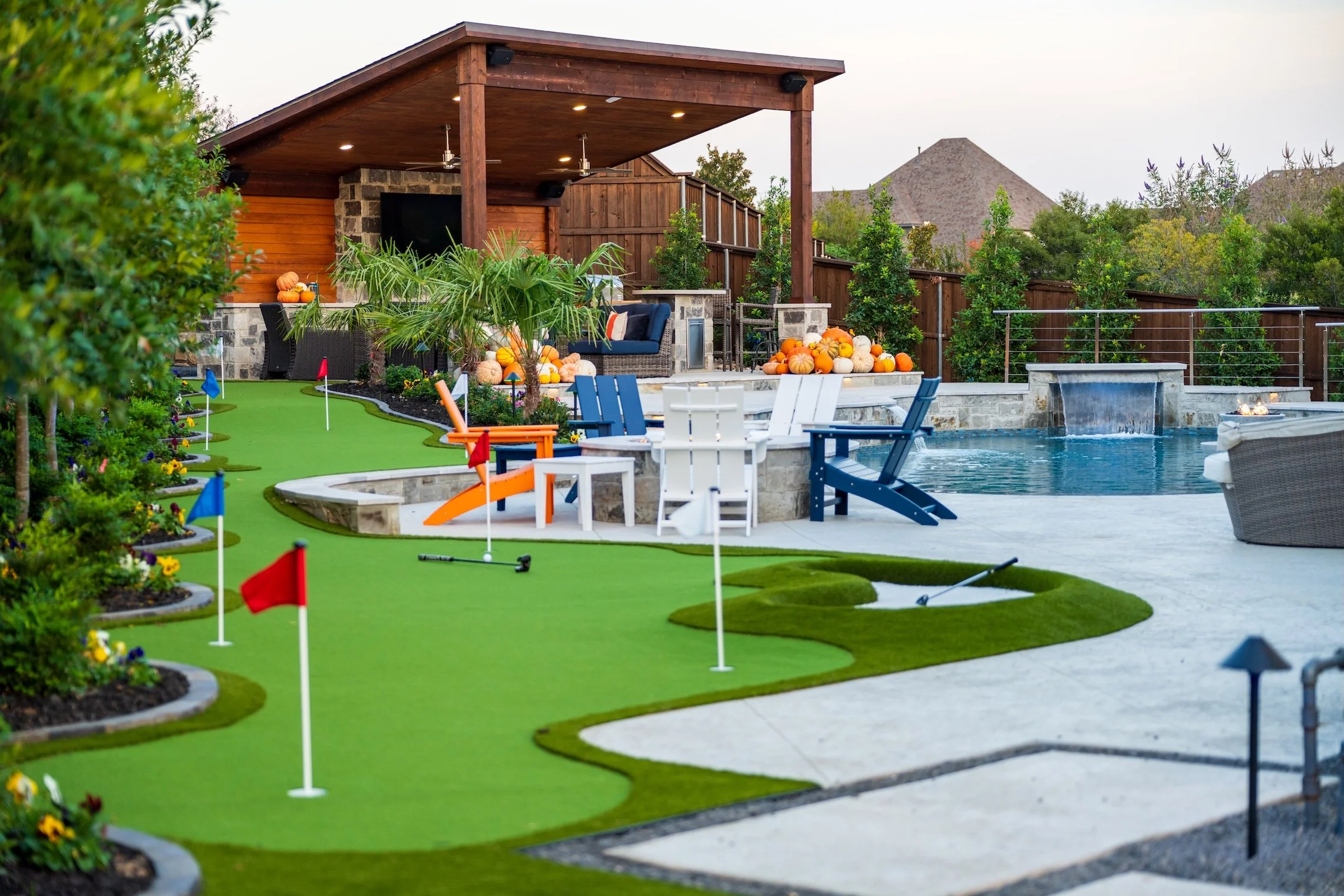 Backyard with a pool, outdoor seating, a shaded patio, and a mini golf putting green decorated with pumpkins and pumpkins.
