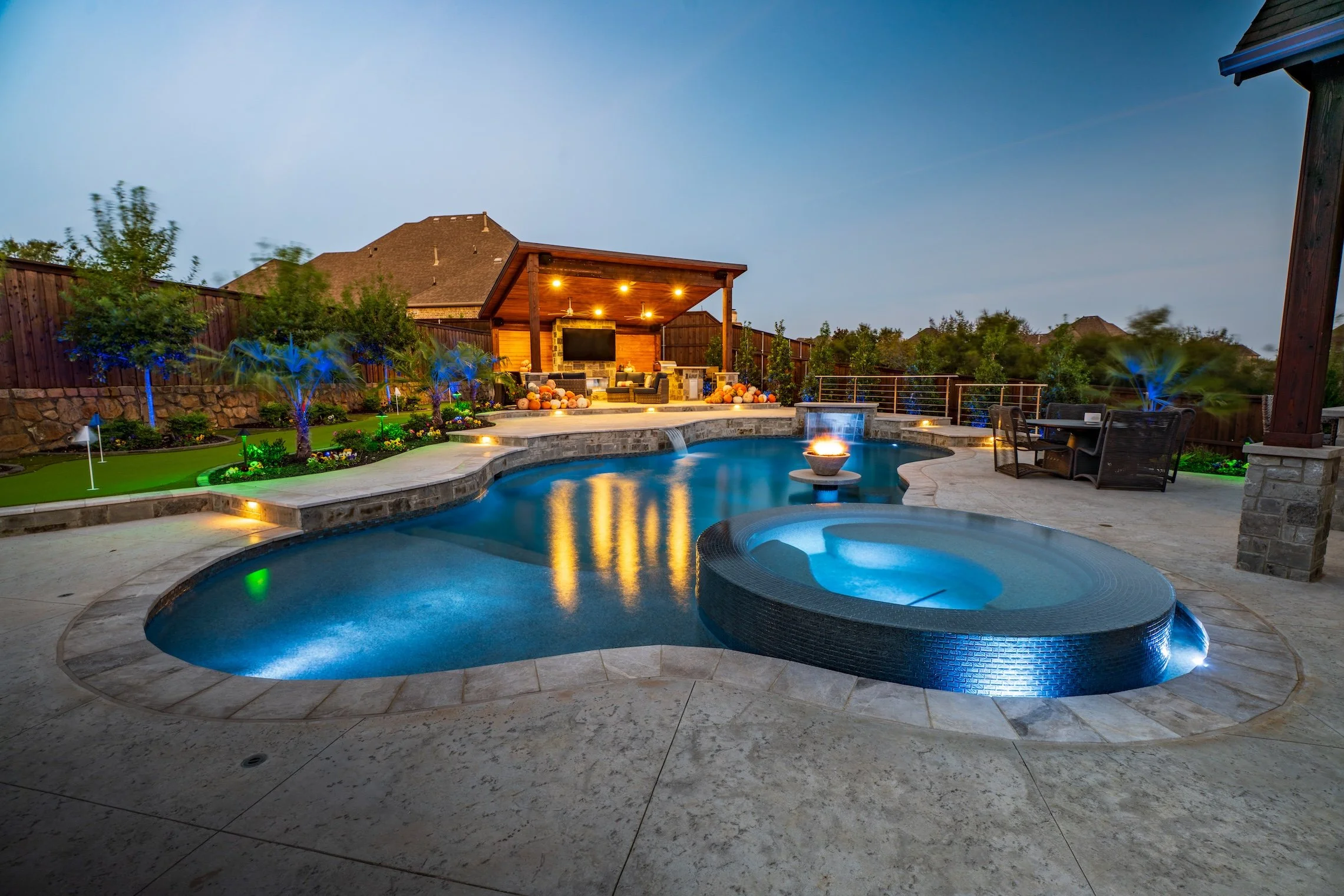A backyard with a swimming pool, hot tub, outdoor seating, and a patio with string lights at dusk.