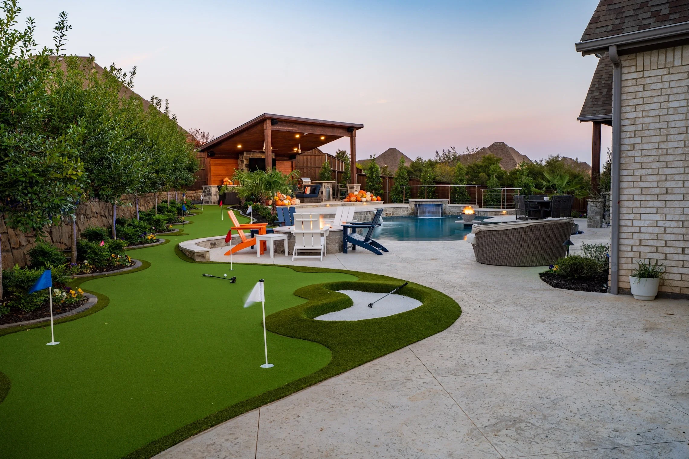 Backyard with putting green, pool, hot tub, outdoor seating and a covered patio at sunset.