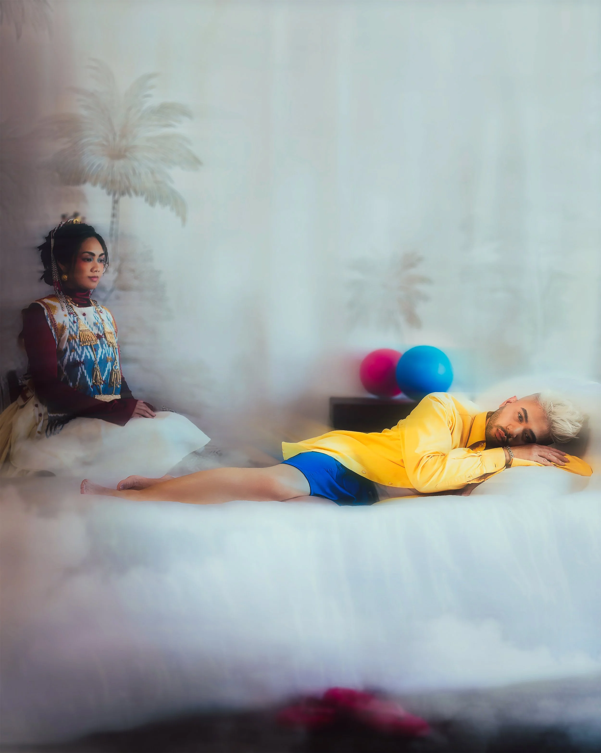 The Babaylan seated at the foot of a bed where the boy lies in a yellow shirt