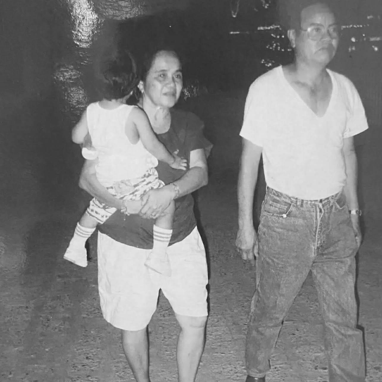 Black-and-white photo of Kyle as a toddler, carried by his grandmother as his grandfather walks beside them at a town carnival in Lubao, Pampanga
