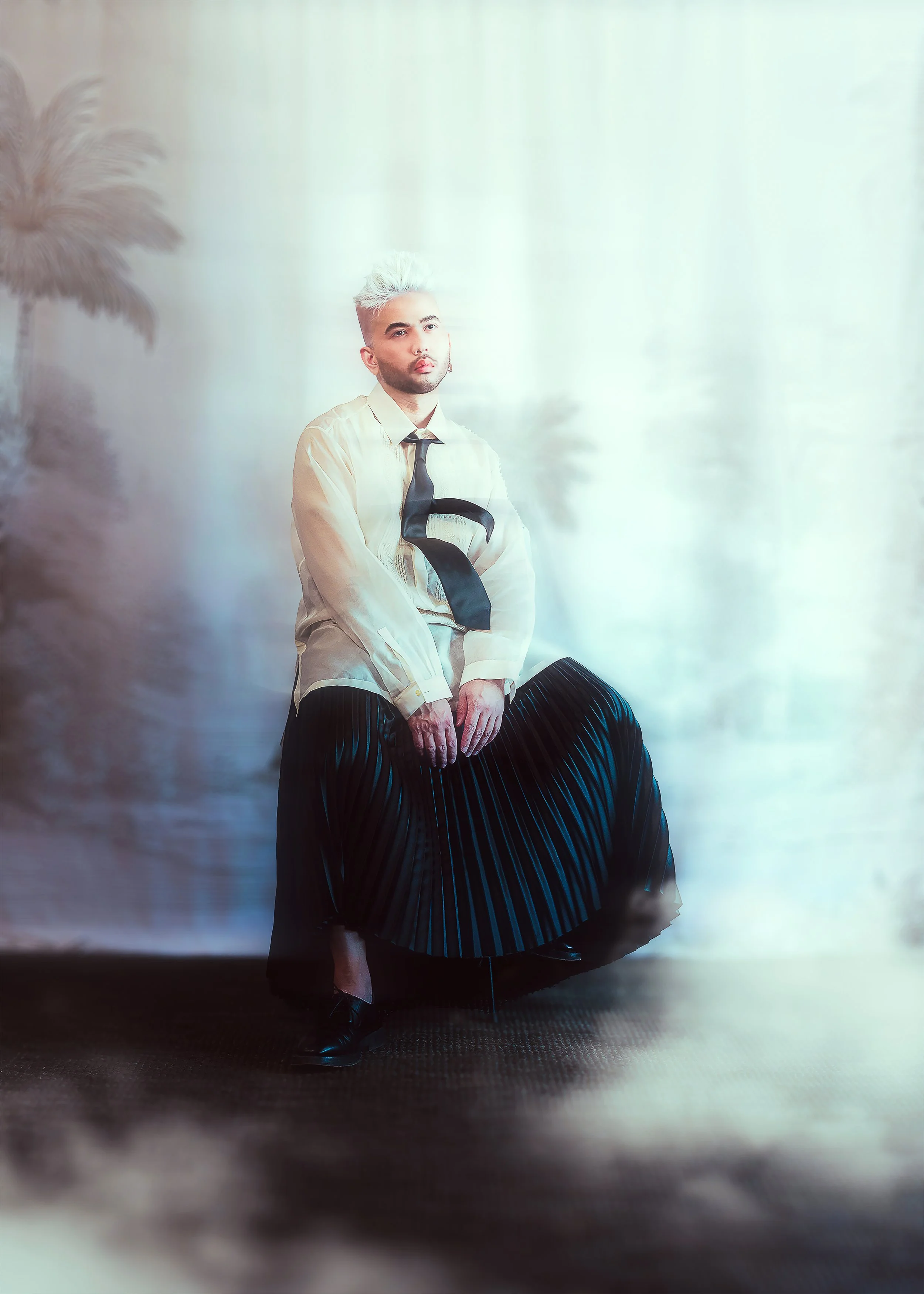 A man in an abaca barong, black tie and pleated skirt, seated