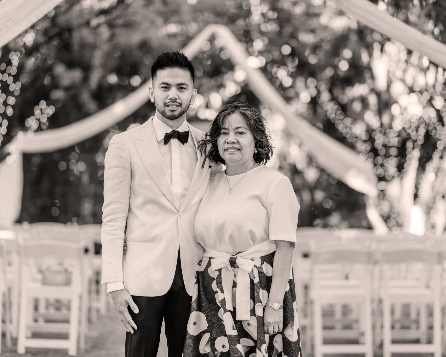 A young man in a tuxedo beside an older woman in a patterned skirt and blouse