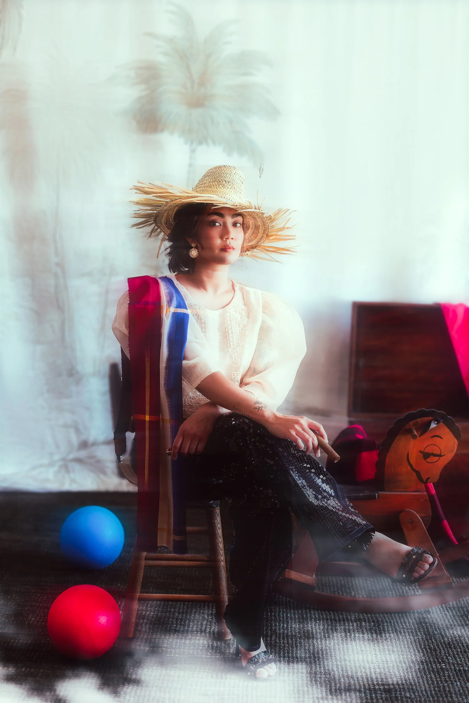 A model in a wide straw hat and sheer blouse, seated, from DIWA's Prologue editorial