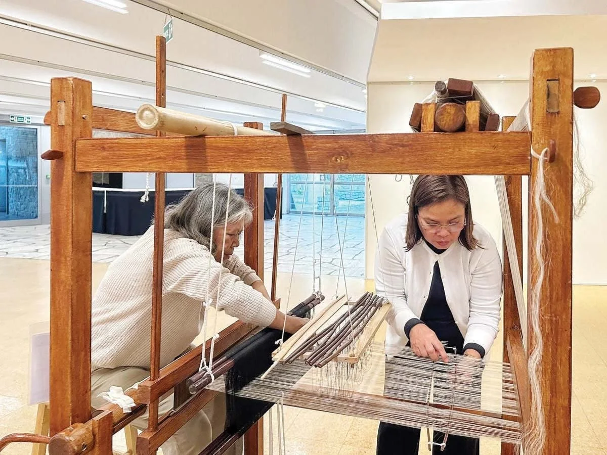 Two women at a cultural institution setting up textile loom