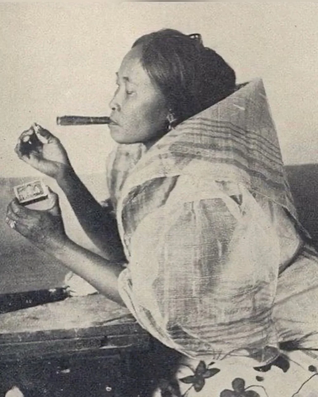 A black-and-white photograph of an Ilocano woman smoking