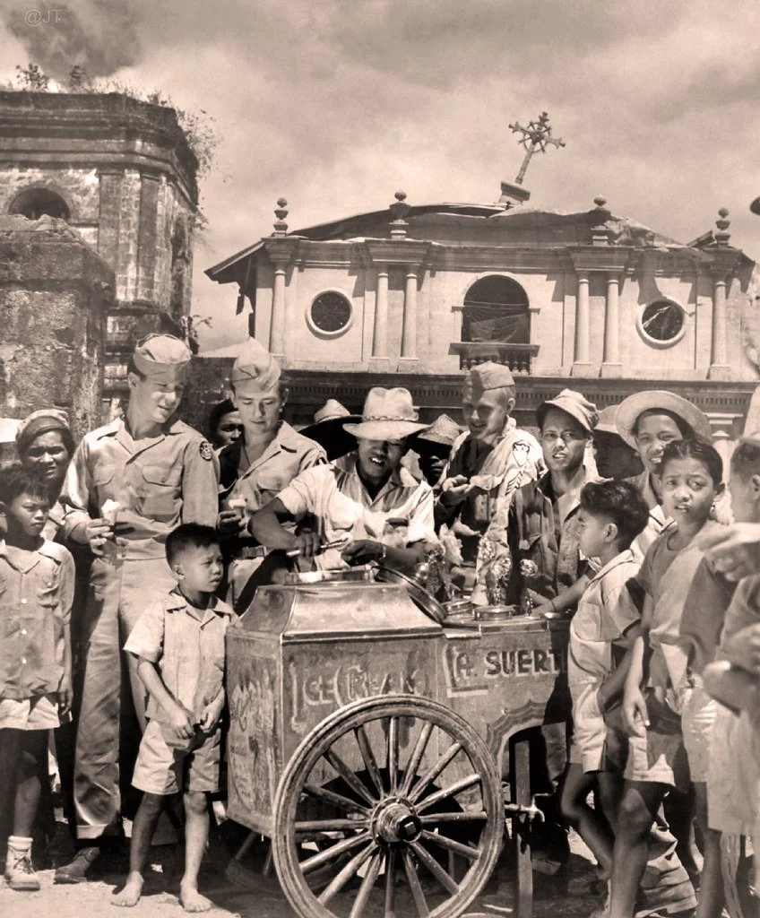 A crowd of children around a street vendor cart surrounded by American soldiers, Pateros