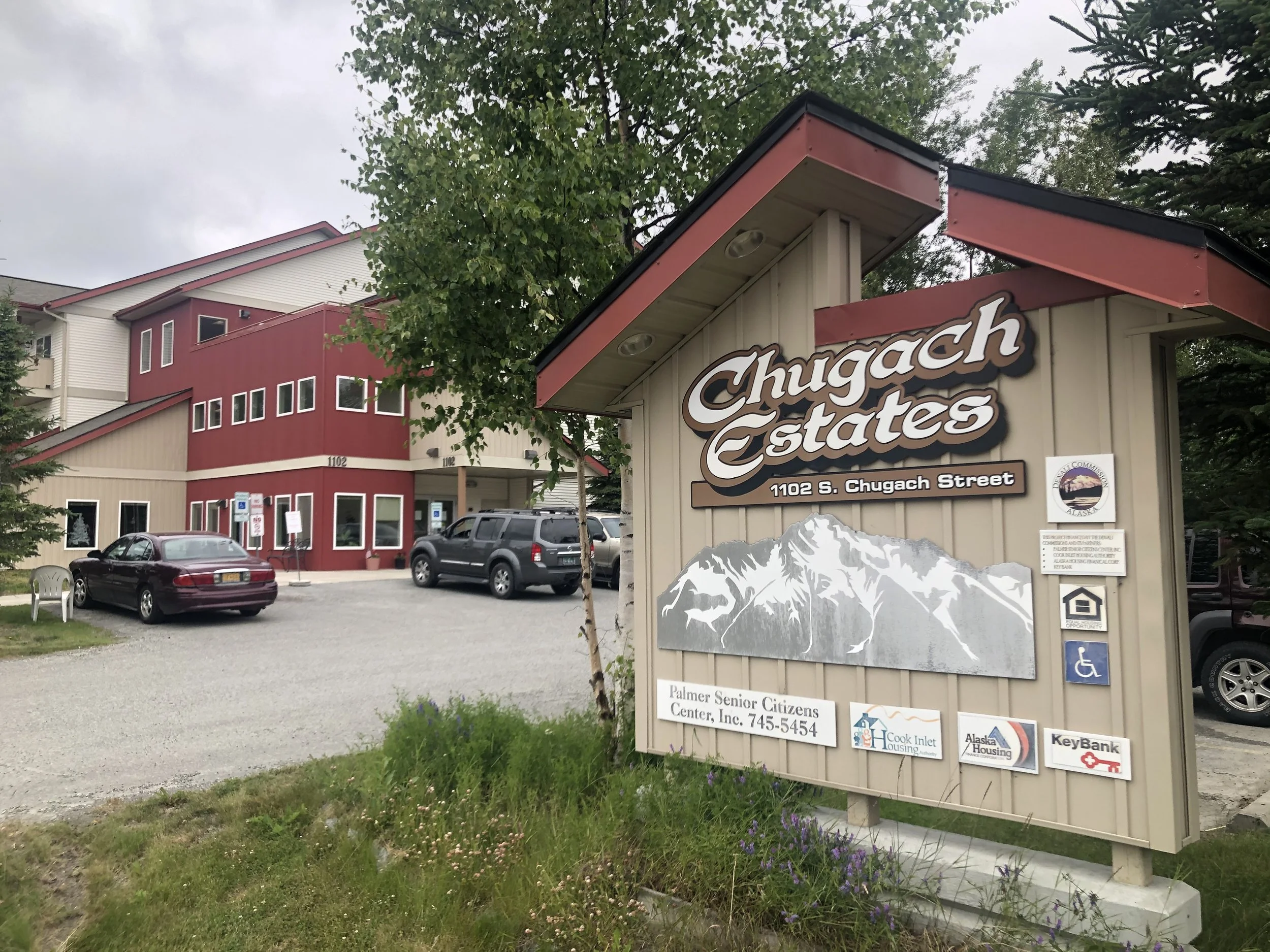 Sign for Chugach Estates with mountain illustration and building in background, located at 1102 S. Chugach Street, Palmer, Alaska.