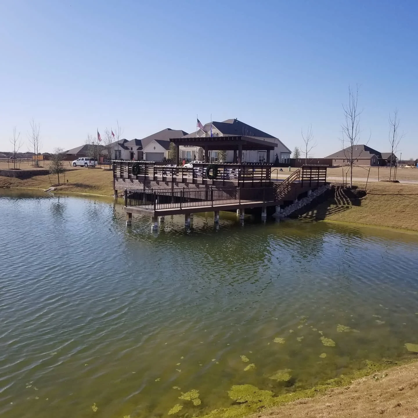 Residential houses with a pond and a wooden deck with stairs and railing in the foreground.