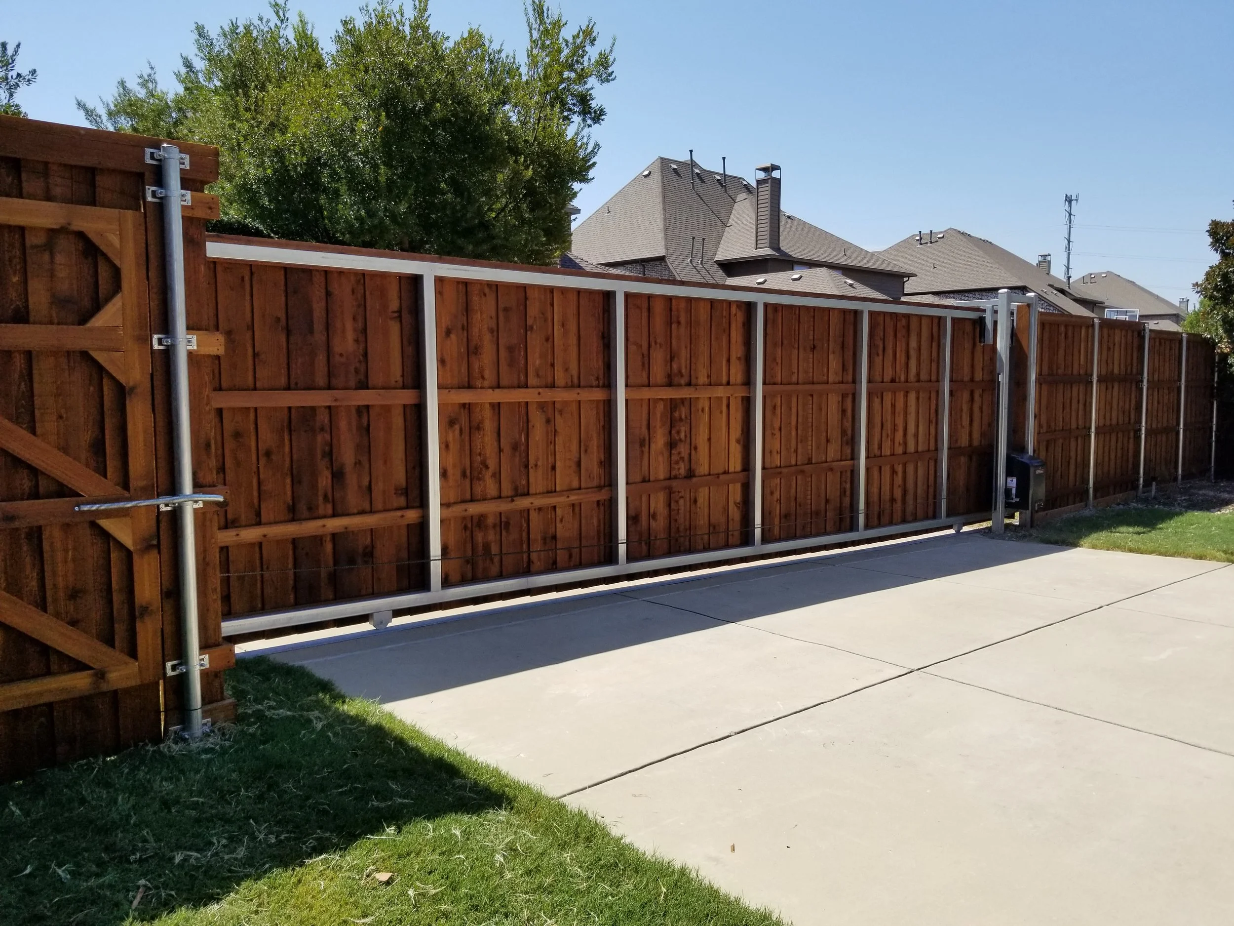 A wooden privacy fence with a sliding gate installed on a concrete patio in a residential backyard.