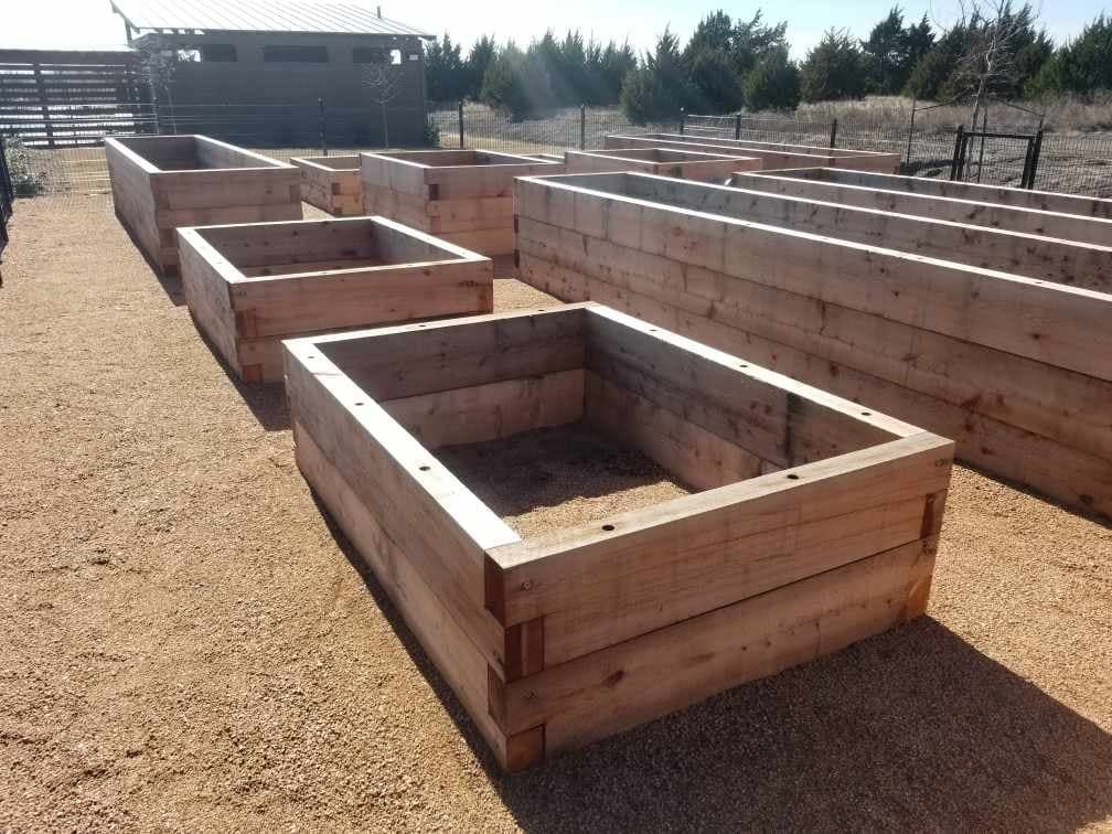 Multiple large wooden raised garden bed frames on a gravel surface outdoors.