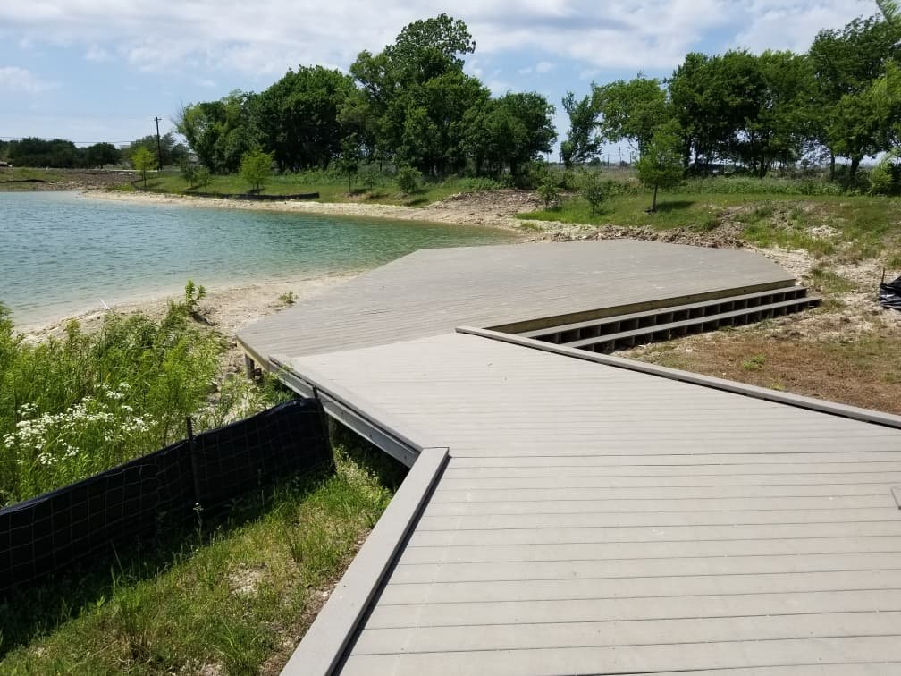 A wooden dock extends into a lake with trees and greenery in the background.