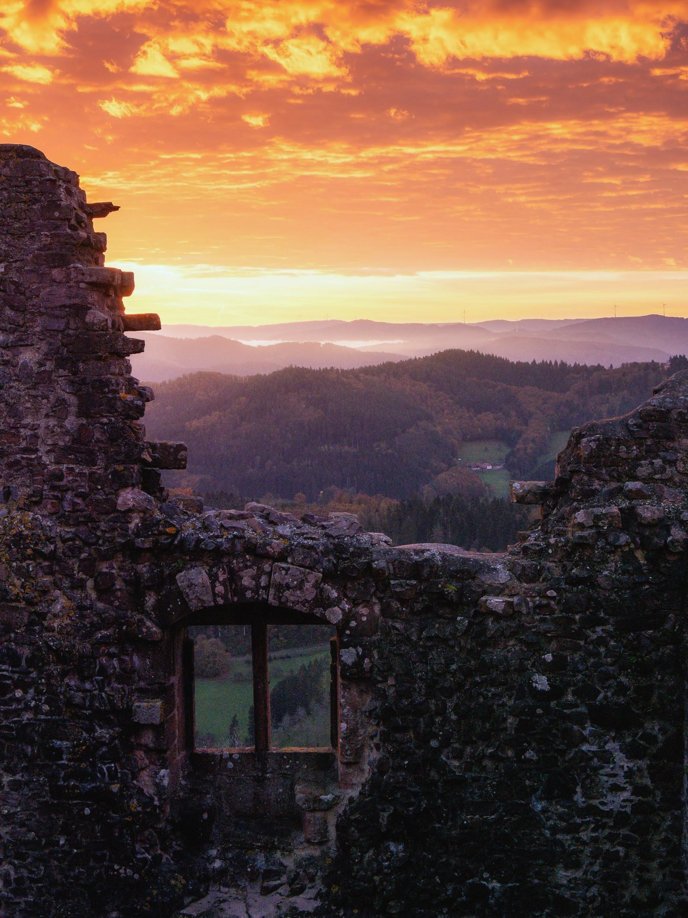 Farbenprächtiger Sonnenaufgang im Schwarzwald, im Vordergrund eine Mauer mit Fenster der Burgruine Geroldseck bei Seelbach