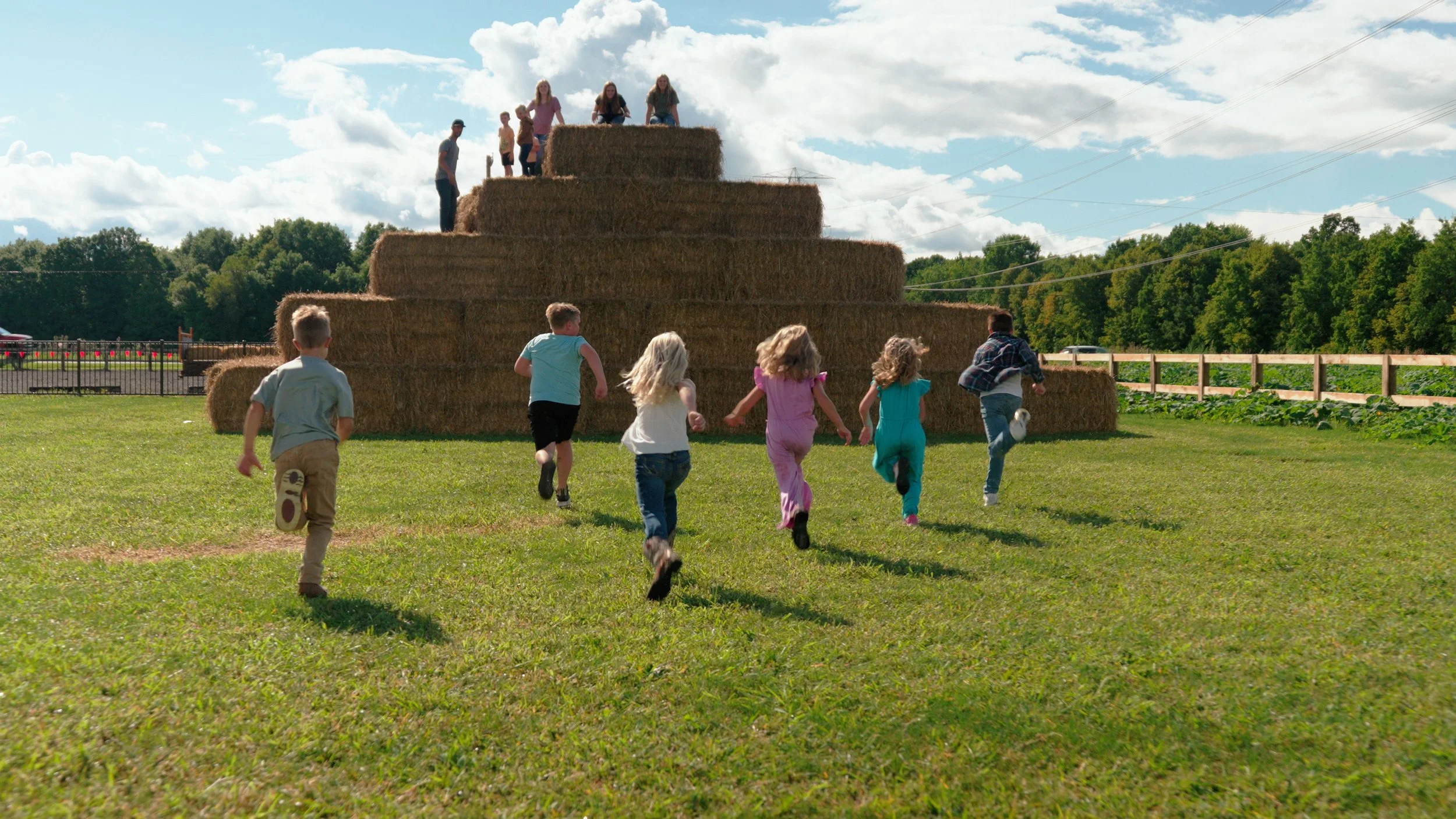 Children running towards a large haystack on a grassy field during daytime.