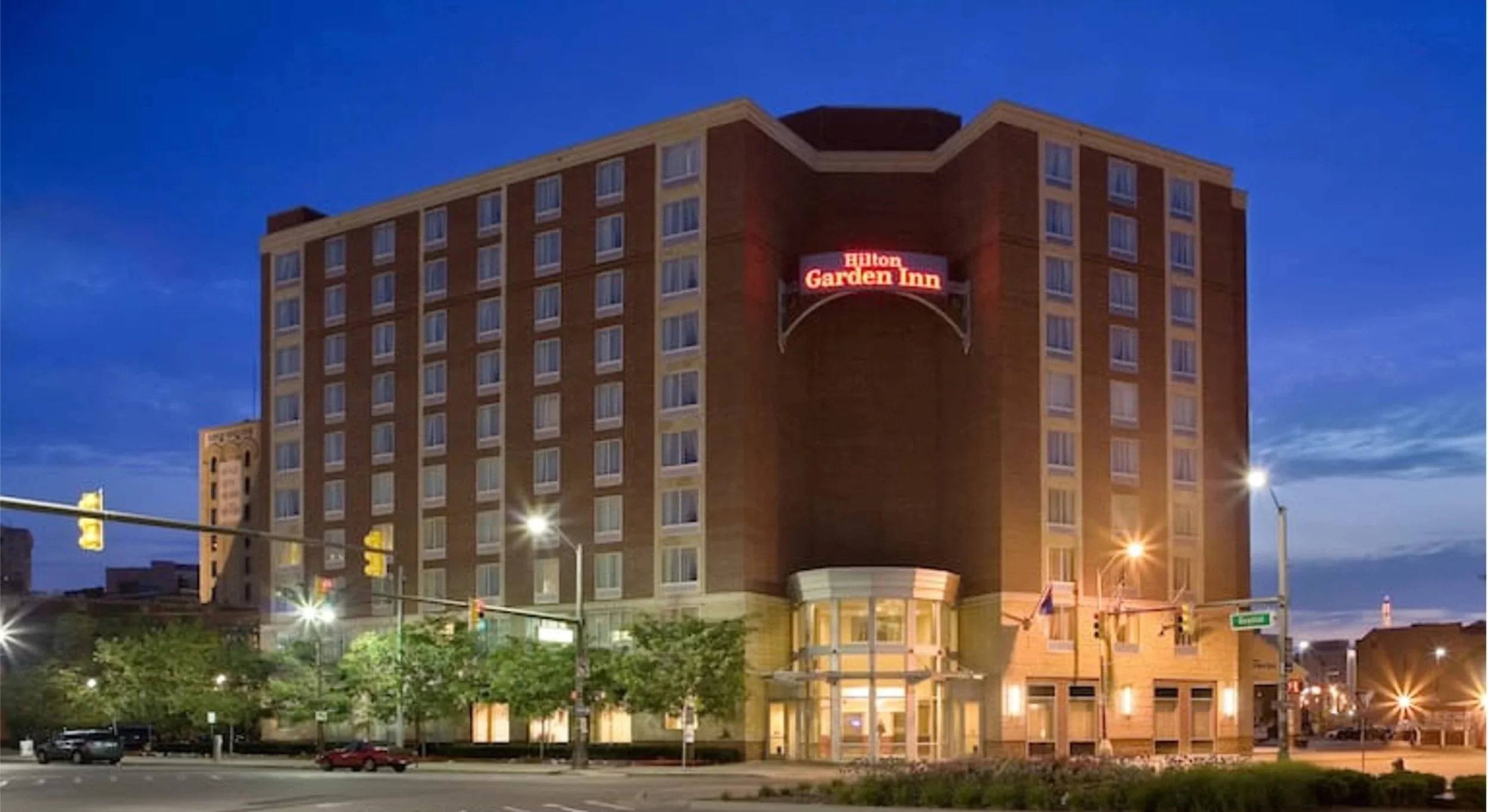 The Hilton Garden Inn hotel building at dusk with illuminated windows and a red glowing sign that reads 'Hilton Garden Inn'.