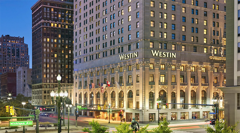 The Westin hotel on a city street corner during evening with illuminated windows and flags, surrounded by tall buildings and streetlights.