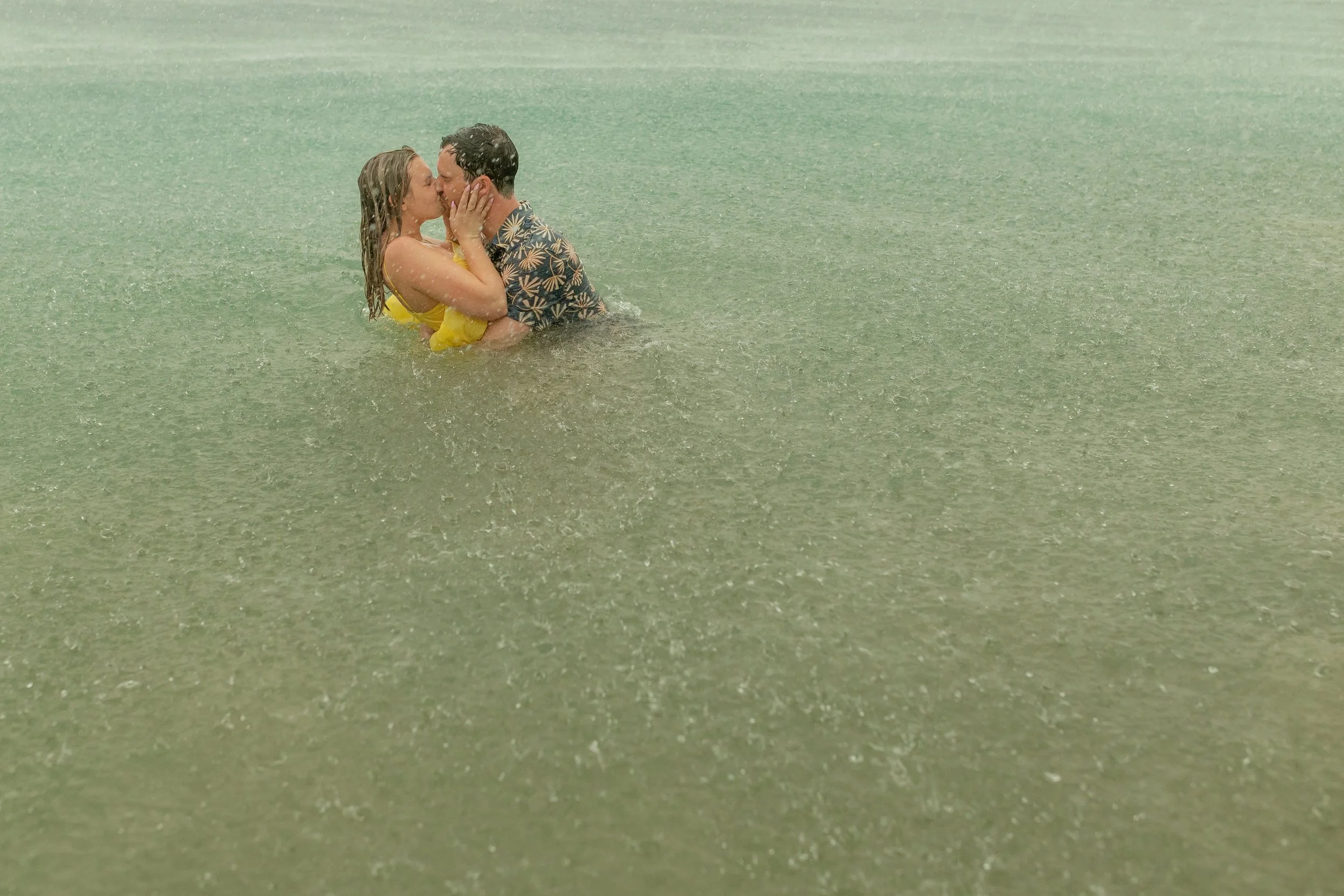 A couple is kissing in the ocean water, holding each other close during a rainy day.