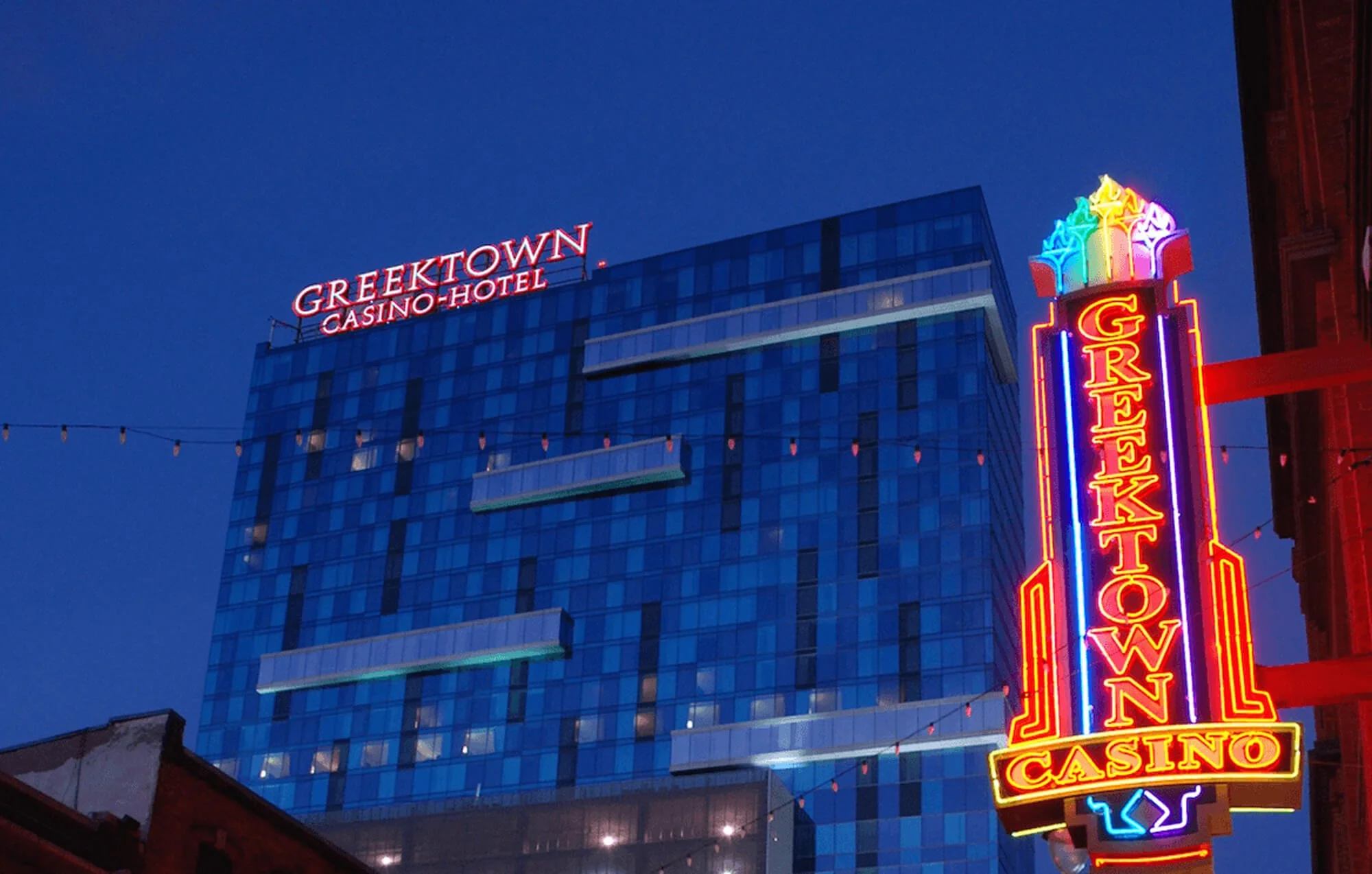 Night view of a city building with neon signs: one for Greektown Casino-Hotel at the top and a large vertical neon sign for Greektown Casino on the right side.