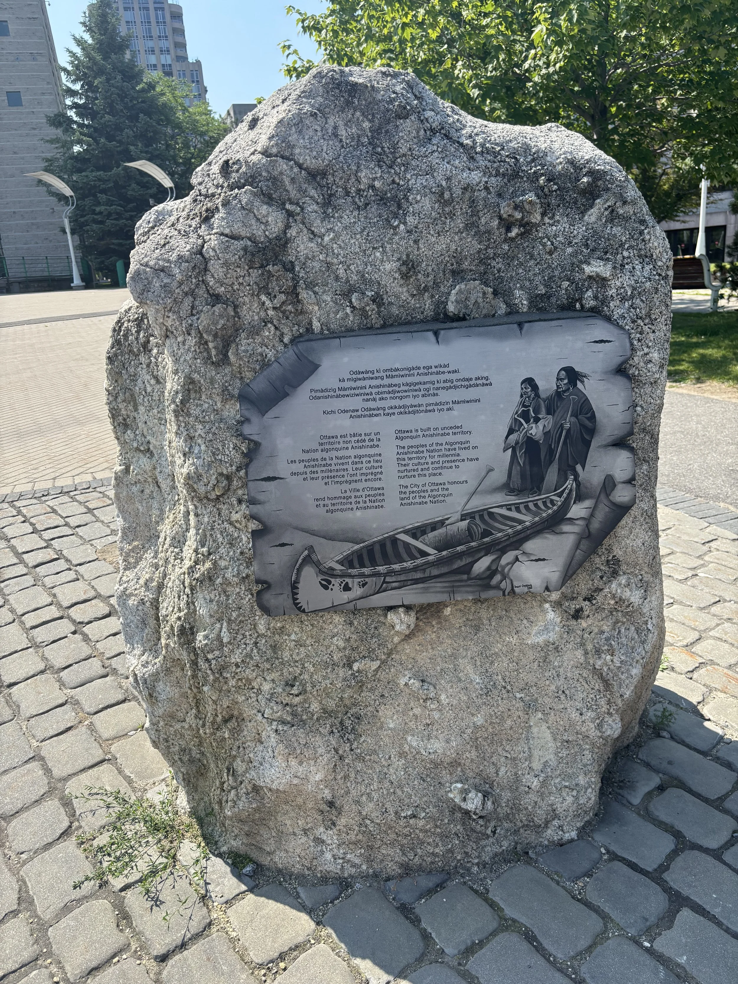 Plate on a large rock describing the history of Ottawa and the Algonquin Anishinabe Nation in English and French, with an illustration of two Indigenous people in traditional clothing and a canoe.
