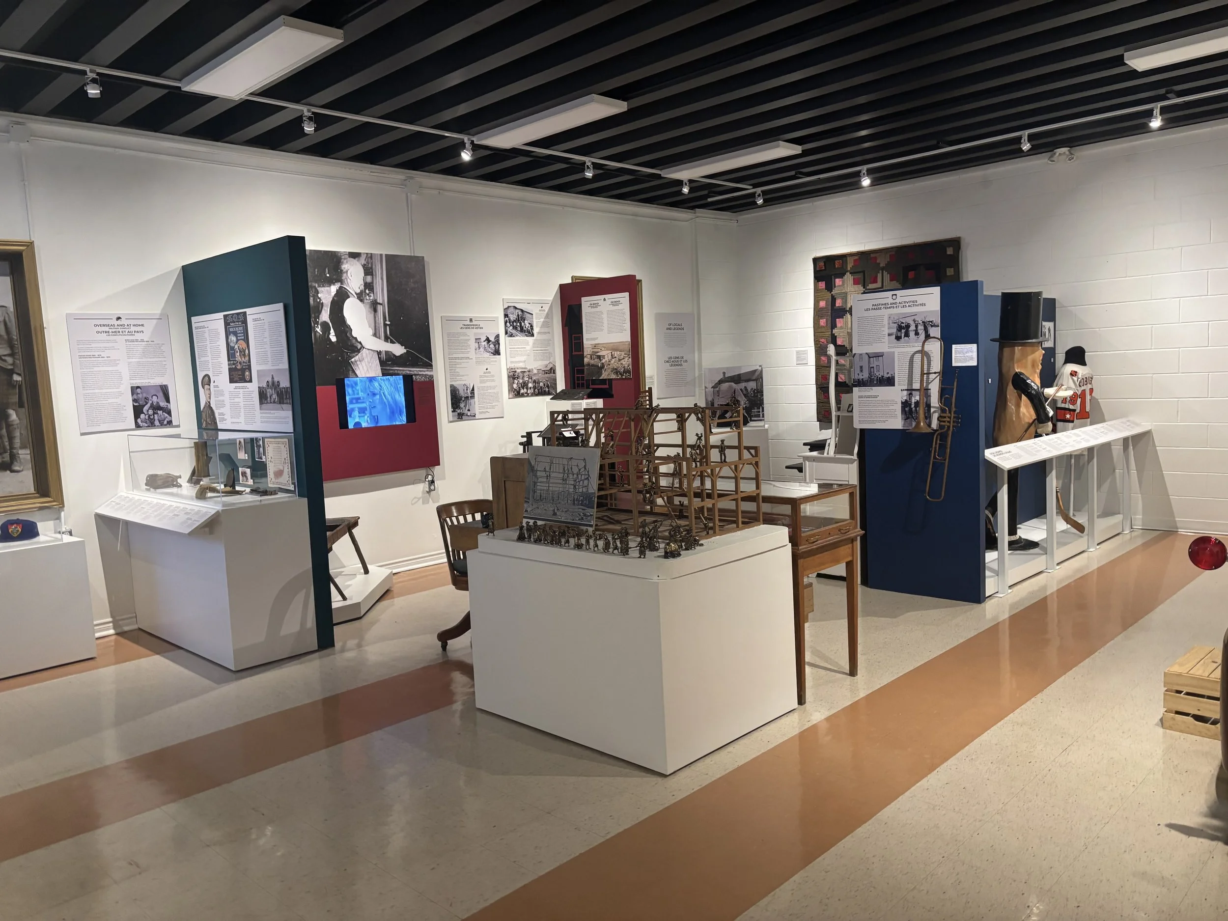 Interior of a museum exhibit with various displays of historical artifacts, photographs, and informational panels on white walls and pedestals.