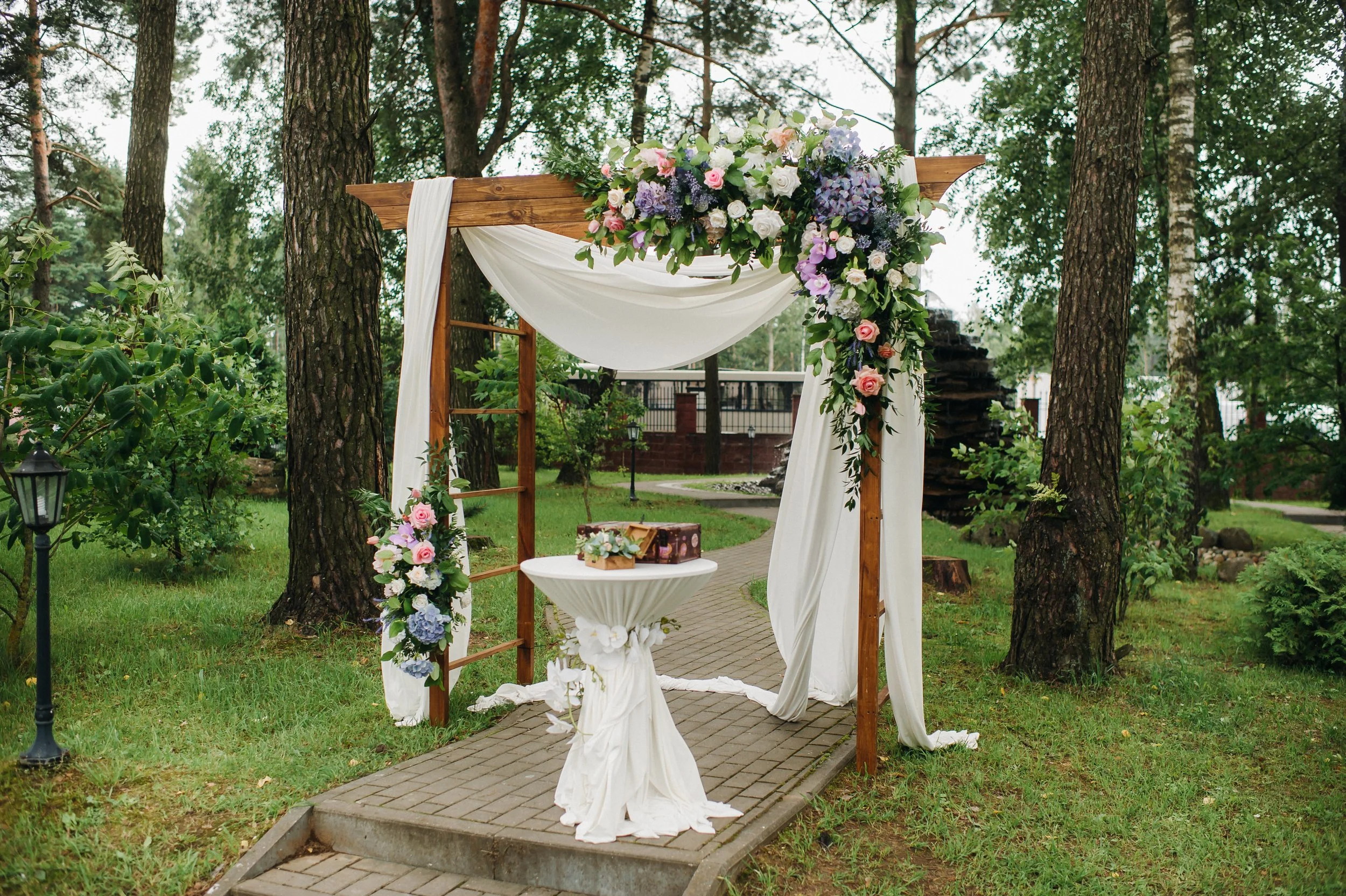 Arche de mariage en bois décoré de fleurs et de tissus blancs dans un jardin bois