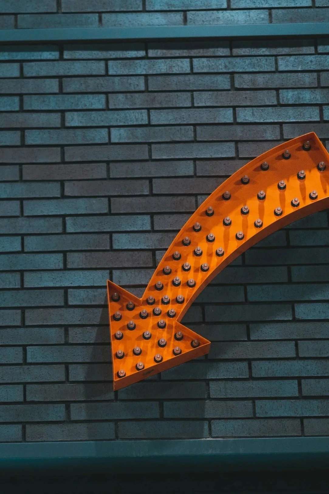 A large orange arrow marquee sign with round light bulbs on a dark brick wall background.