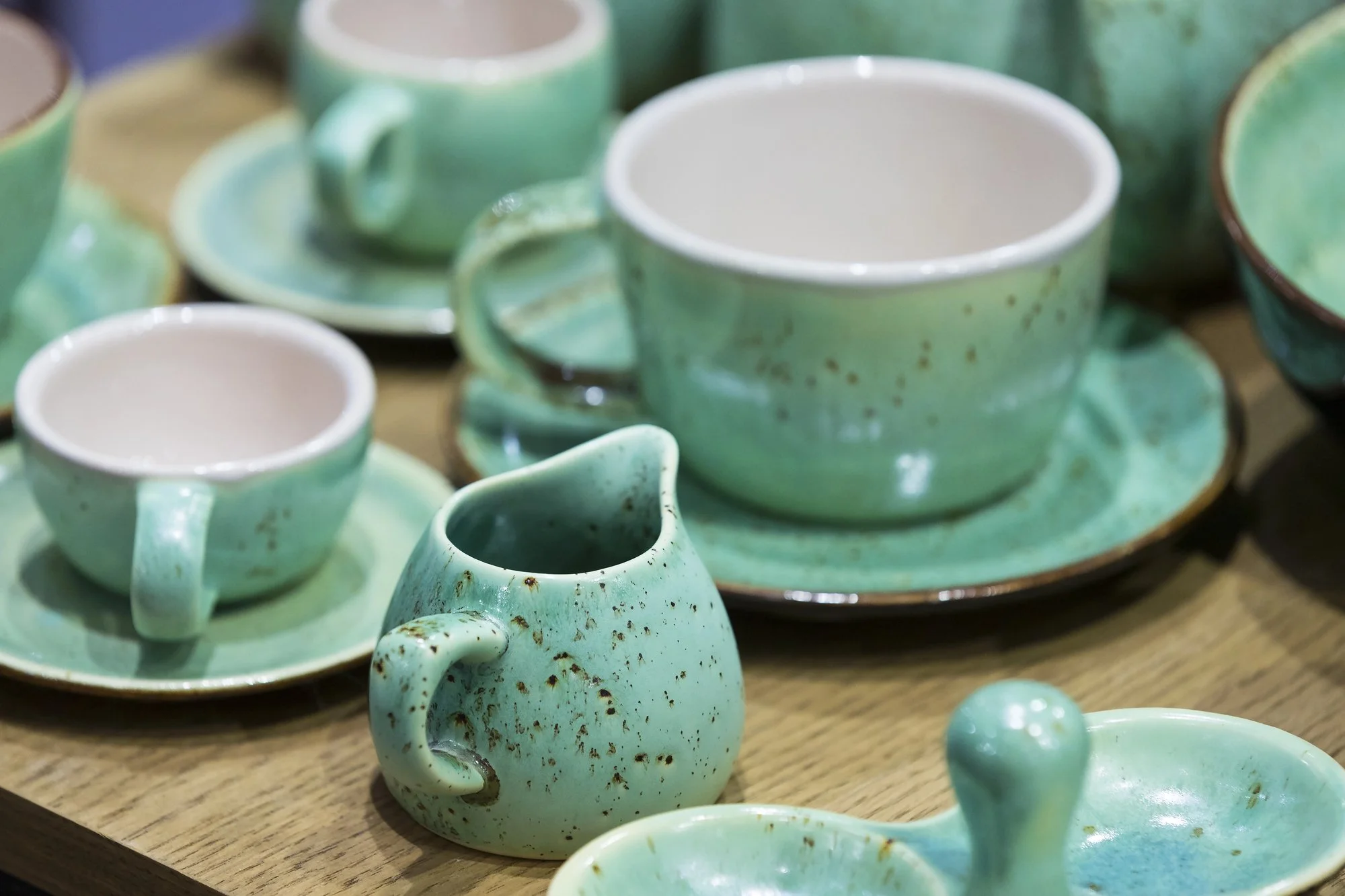 Collection of green glazed ceramic pottery cups, saucers, and a small pitcher displayed on a wooden surface.