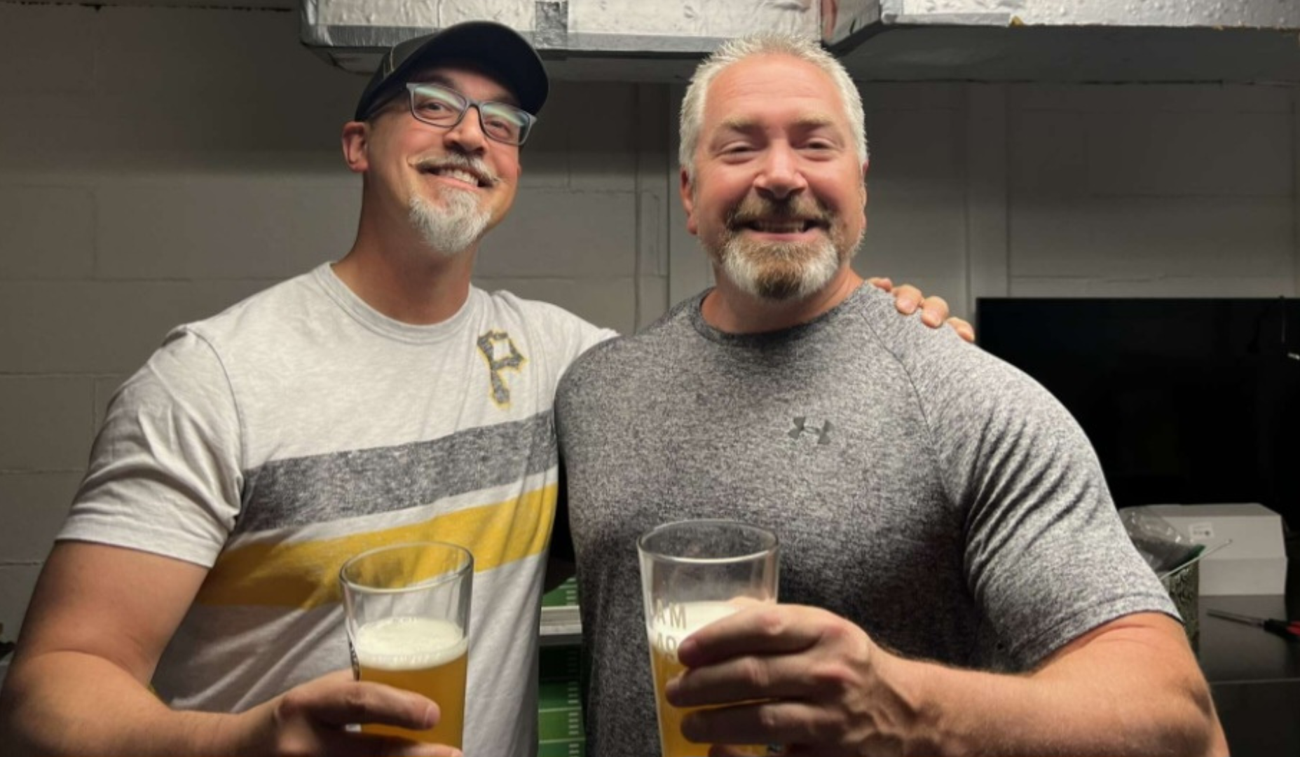 Two smiling men holding glasses of beer in an indoor setting.
