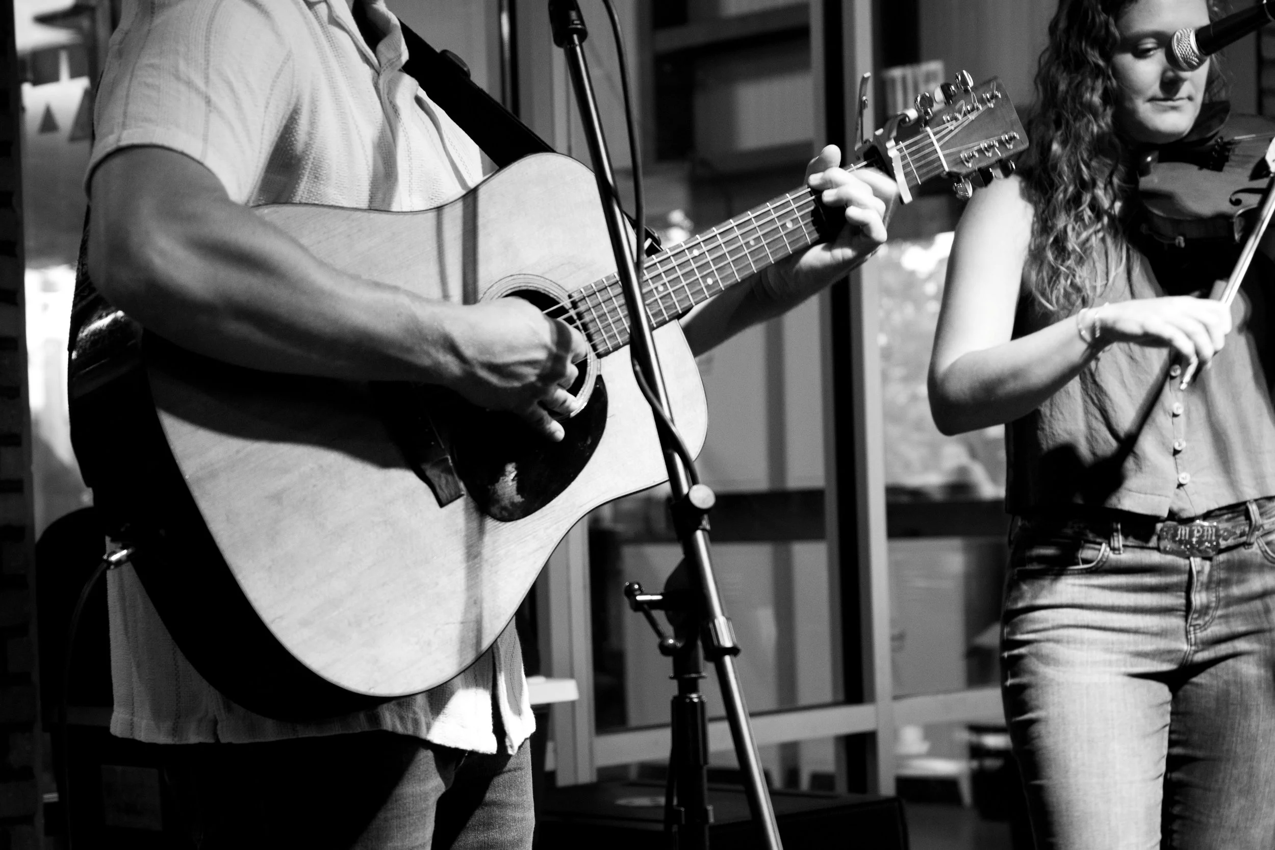 A man playing an acoustic guitar and a woman playing a fiddle during a musical performance.