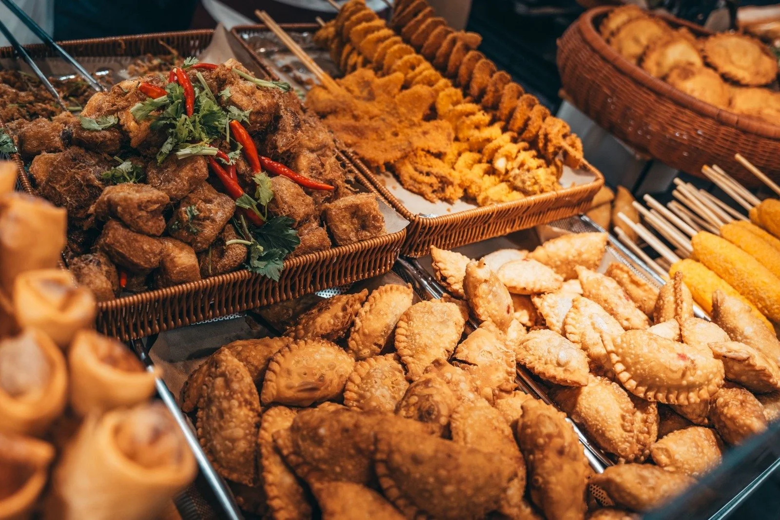 Various fried foods including chicken wings, skewered meat, and other battered items displayed in woven baskets.