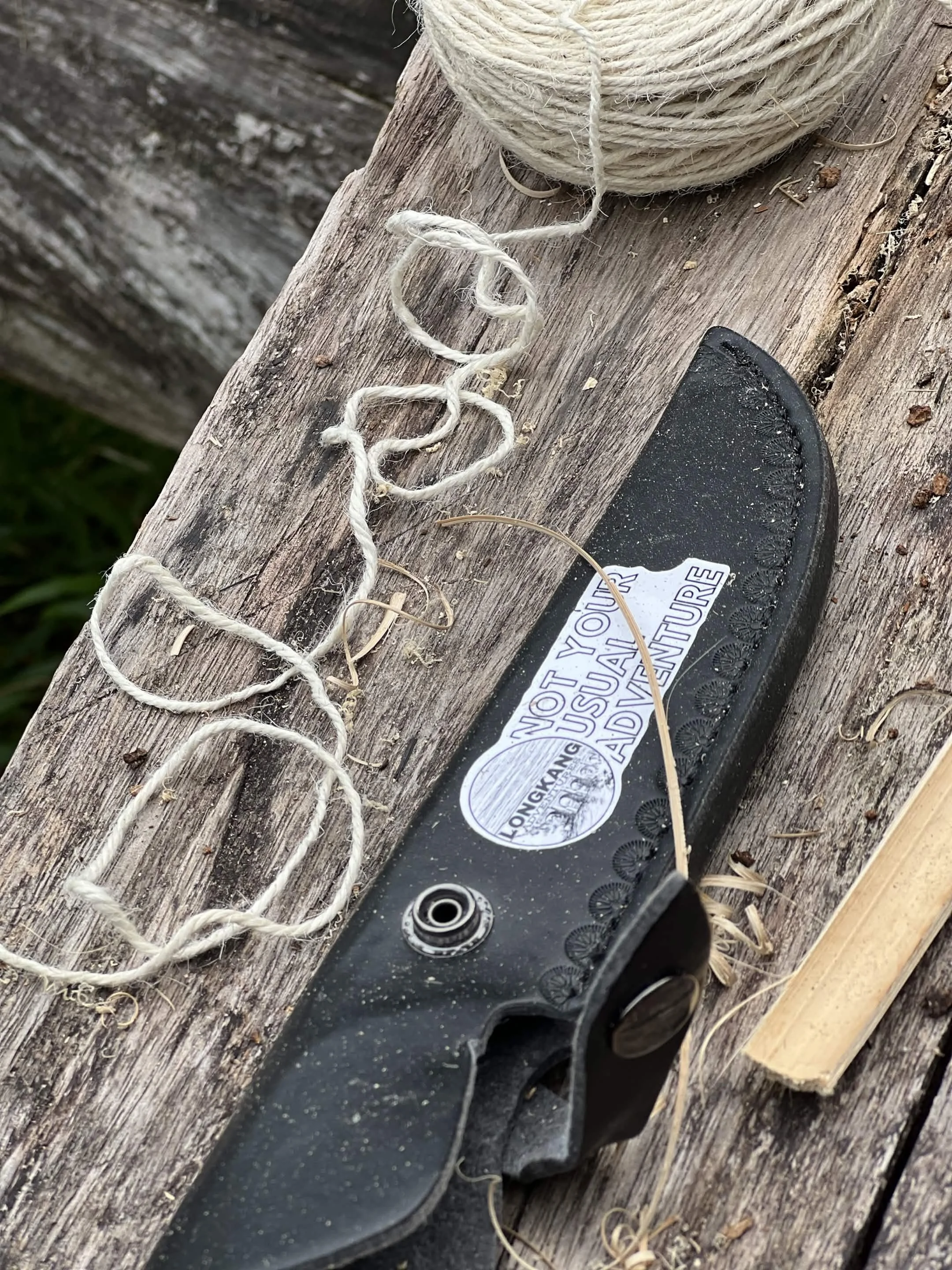 Close-up of a black skateboard deck with a label, lying on a weathered wooden surface, next to a spool of off-white twine.