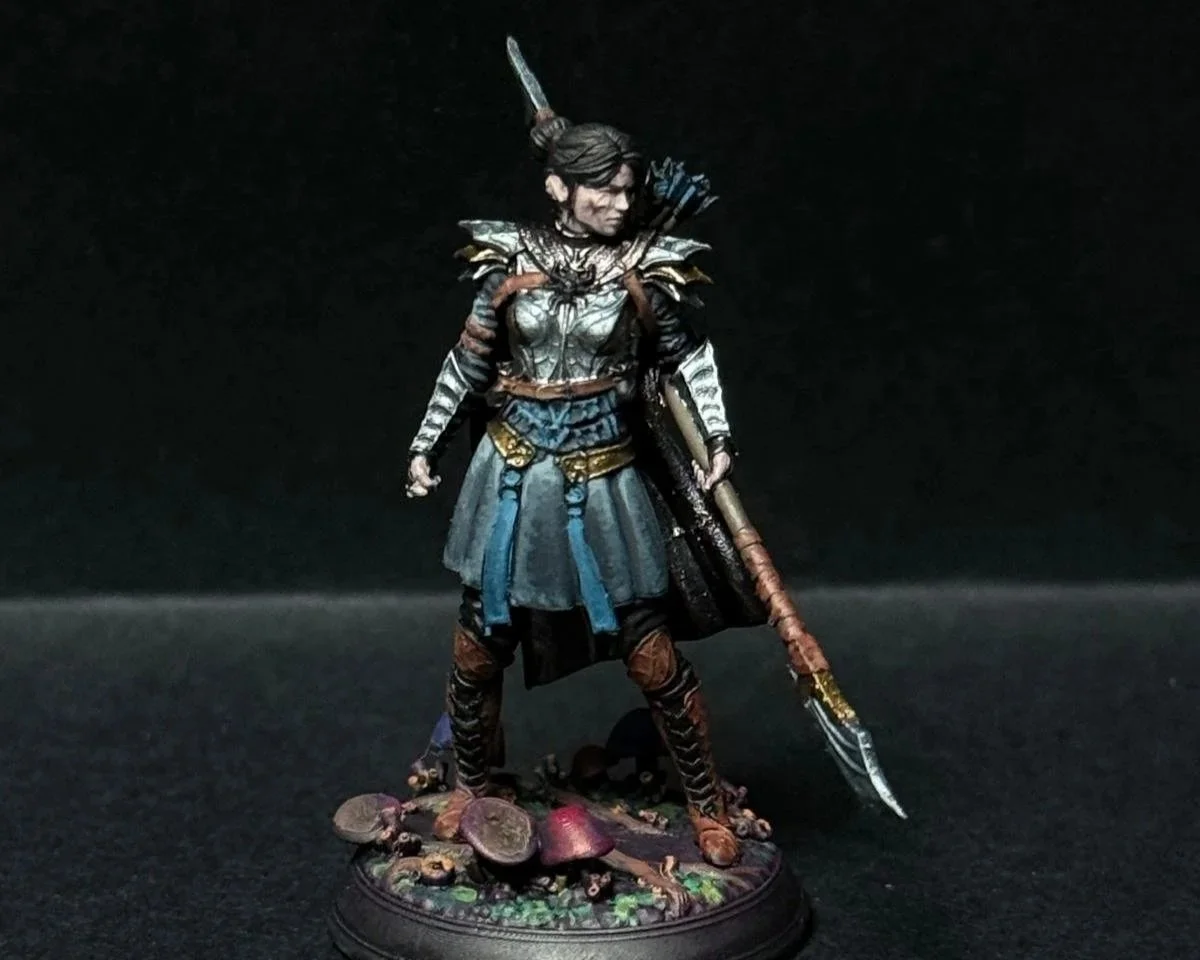 A detailed figurine of a female warrior with armor, a cape, and a spear, standing on a base decorated with mushrooms and plants.
