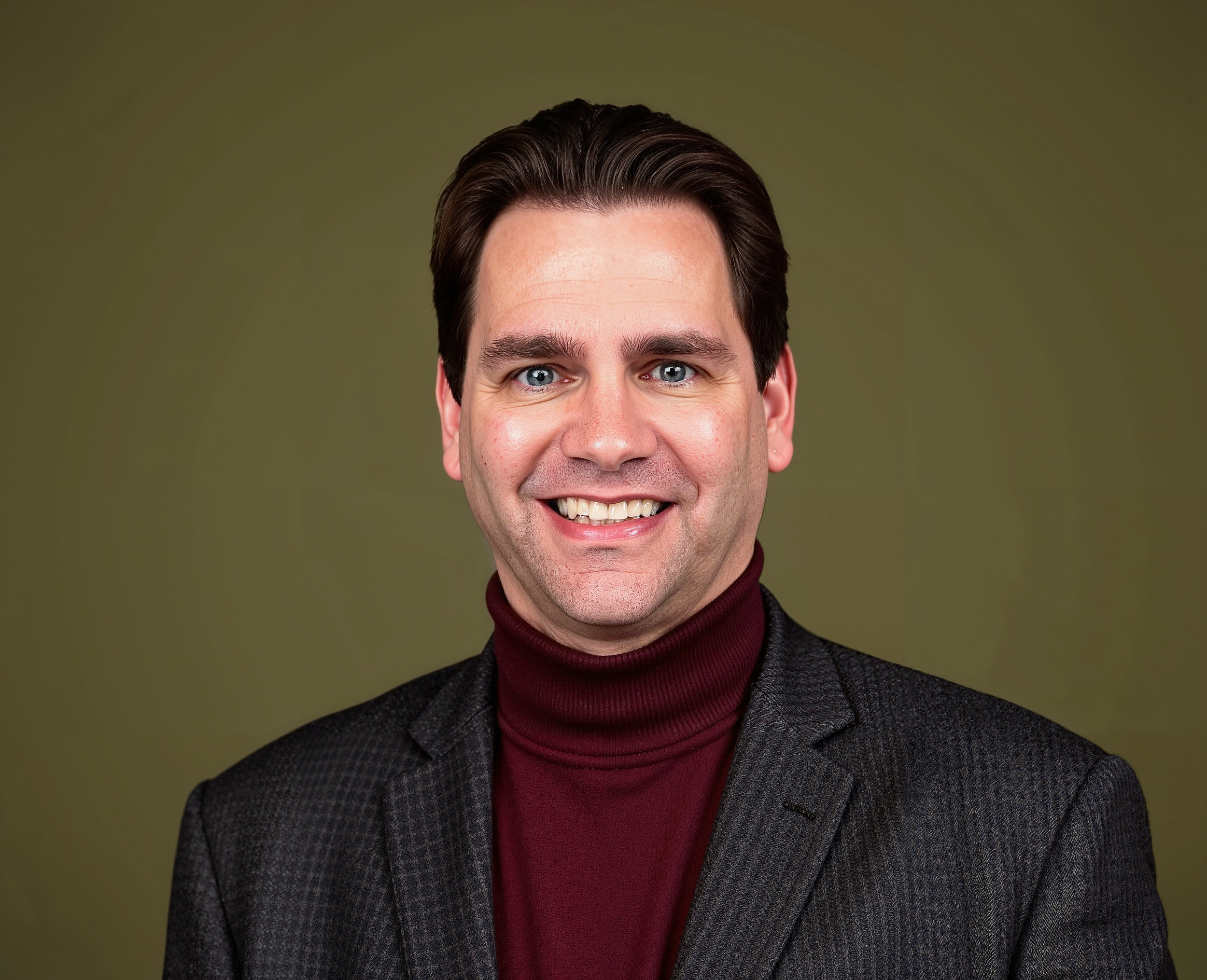 a man headspot smiling in a deep red turtle neck and brown suit
