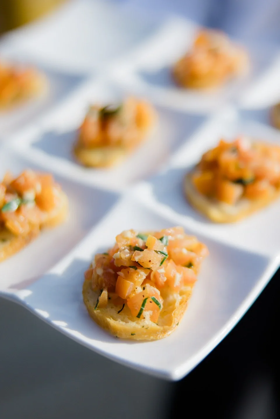 Close-up of canapé bites topped with chopped smoked salmon and herbs, arranged on a white serving tray.
