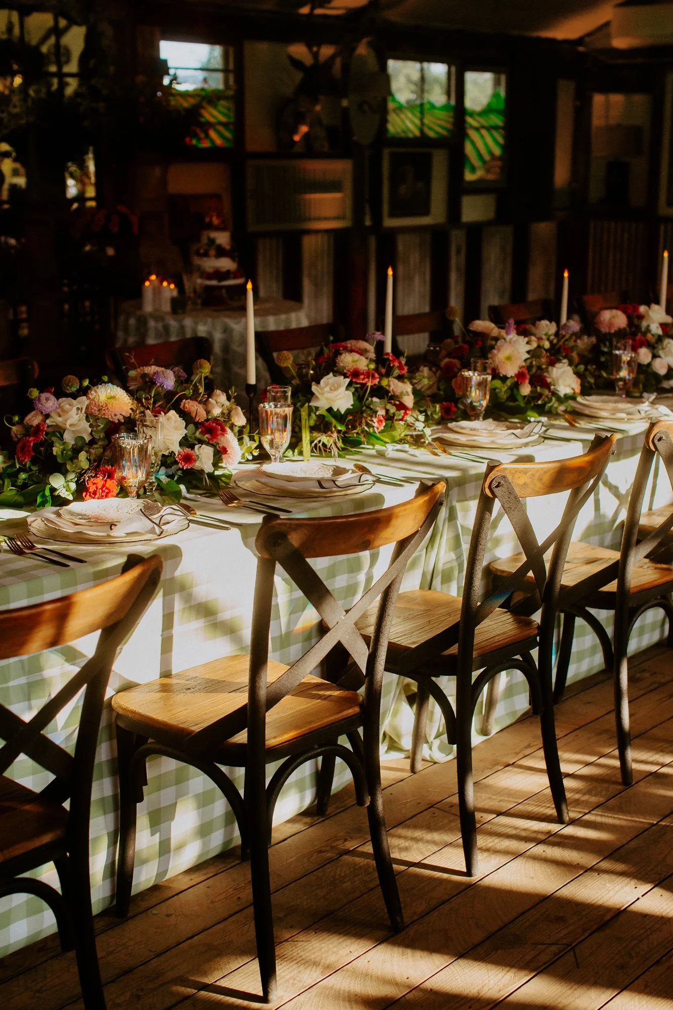 Elegant dining table set for a special occasion with floral centerpieces, white candles, and champagne glasses in a rustic venue with checkered tablecloths.