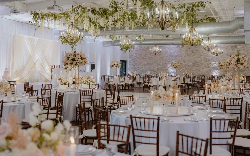 Elegant banquet hall decorated with white drapery, hanging chandeliers, and floral arrangements for a wedding or event.