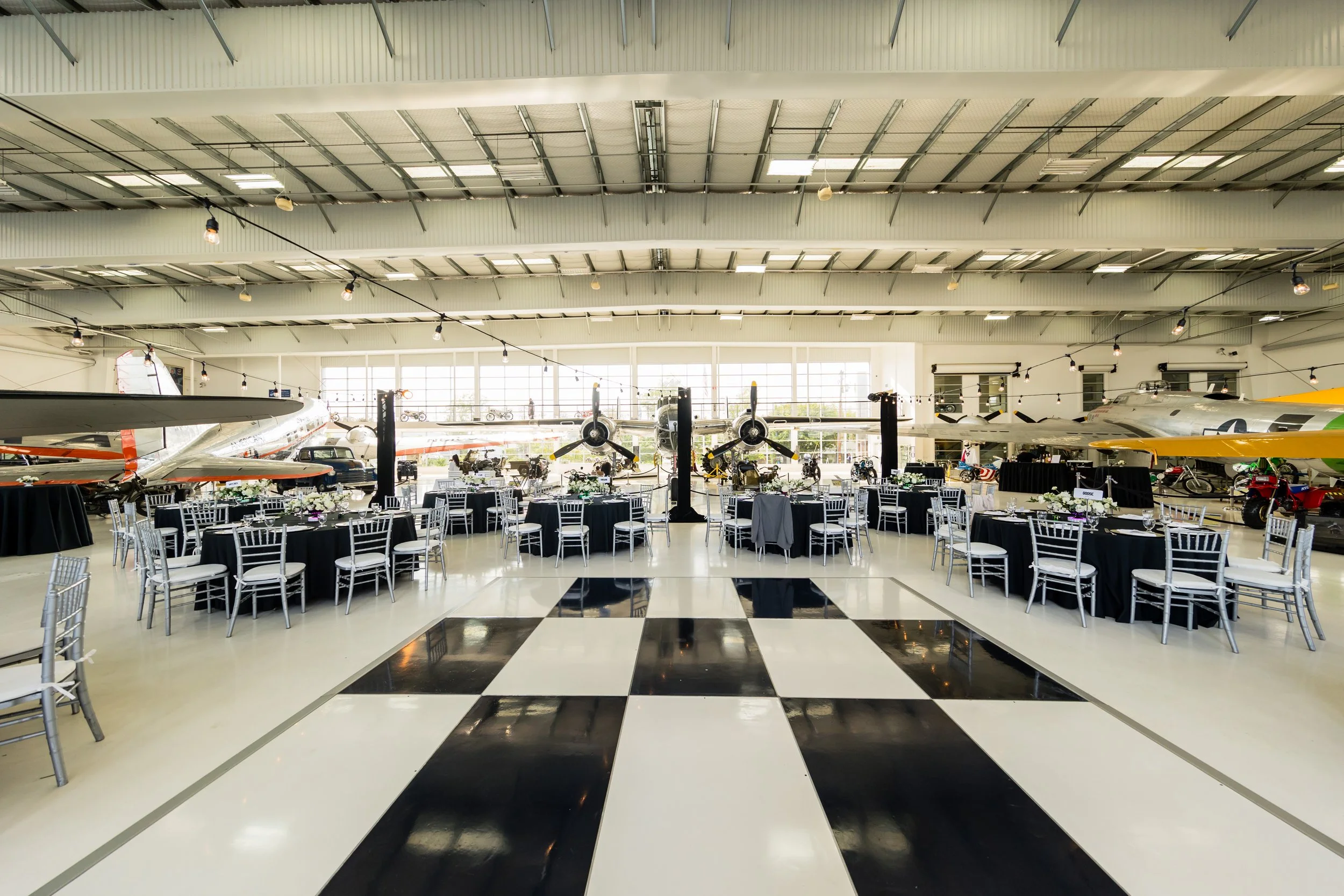 Event setup inside an aviation museum with tables and chairs, surrounded by vintage airplanes and aircraft memorabilia.