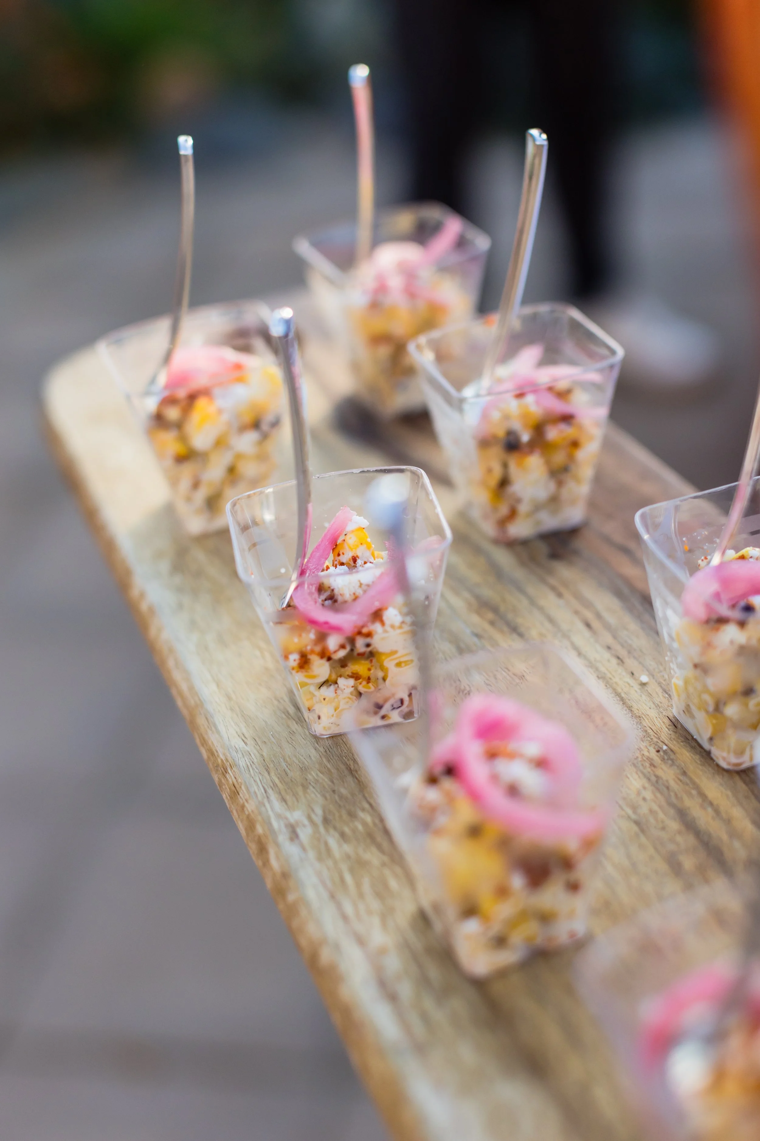 Miniature dessert cups with layered sweet treats topped with pink decoration, served on a wooden surface.