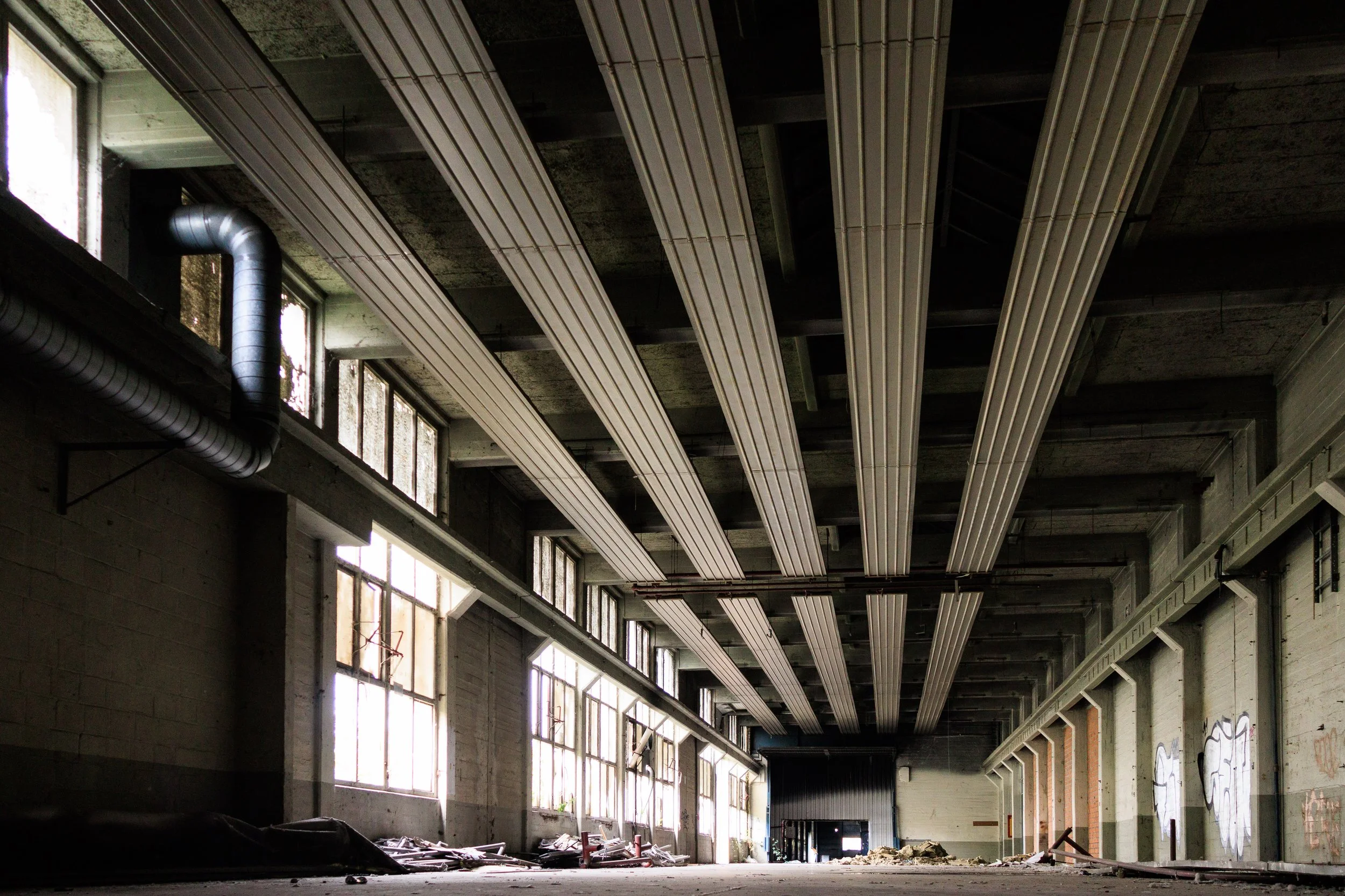 Inside an abandoned industrial building with broken windows, graffiti on walls, and debris on the floor.