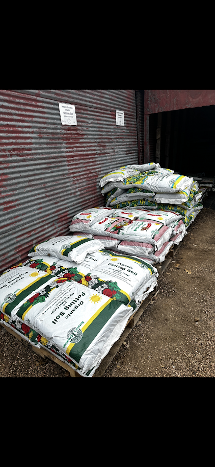 Stacked bags of planting soil next to a corrugated metal wall with signs, outdoors.
