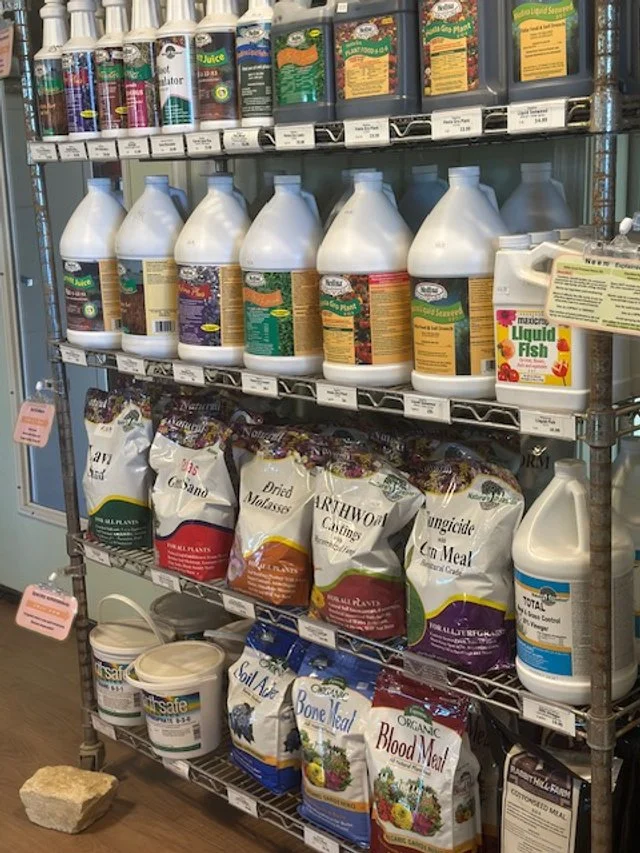 Shelf with various gardening and pest control products, including liquid fish fertilizer, insecticide sprays, and bags of dried seeds or soil amendments.